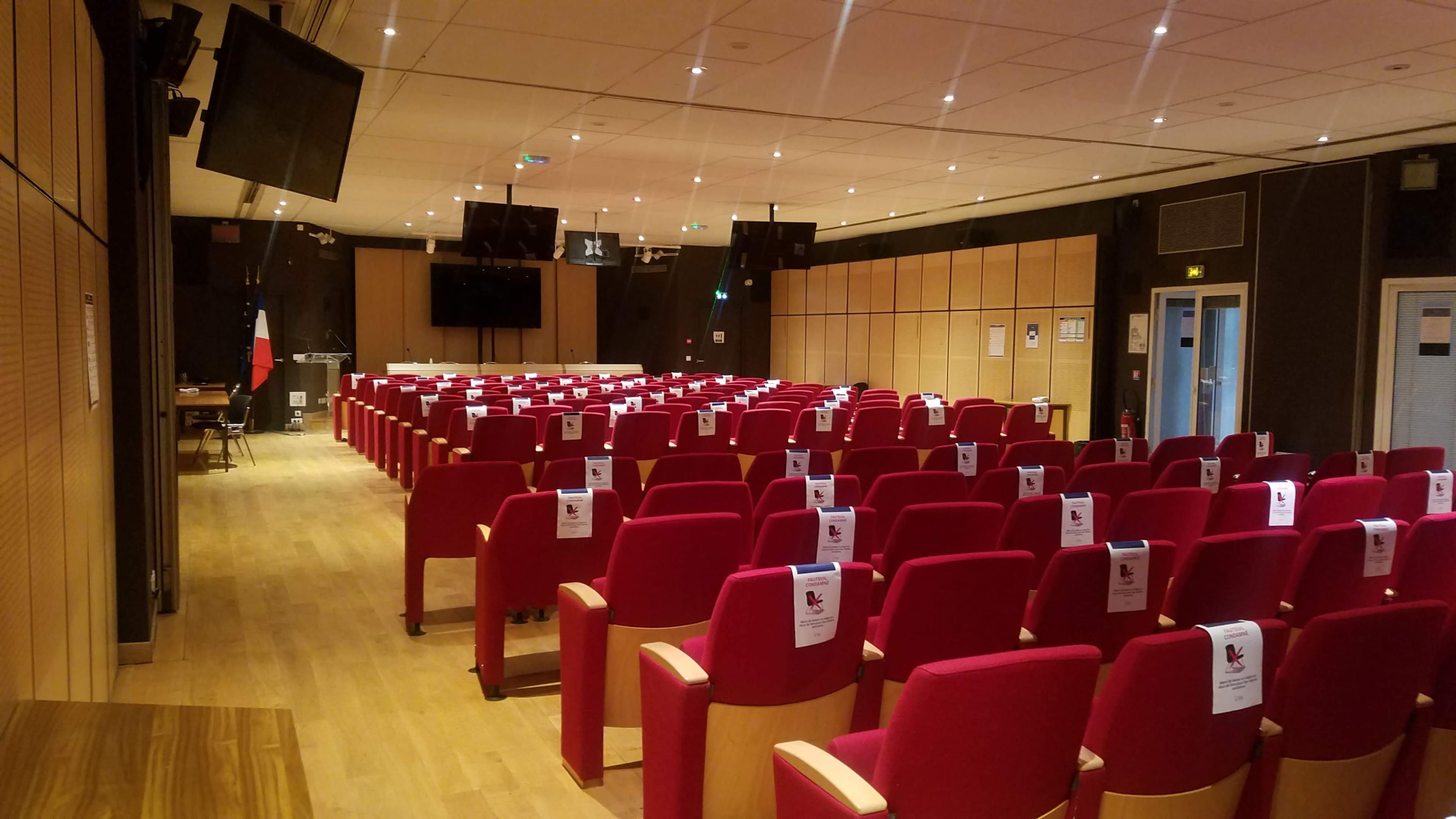 An empty conference room with red chairs arranged in rows and signage on each chair.