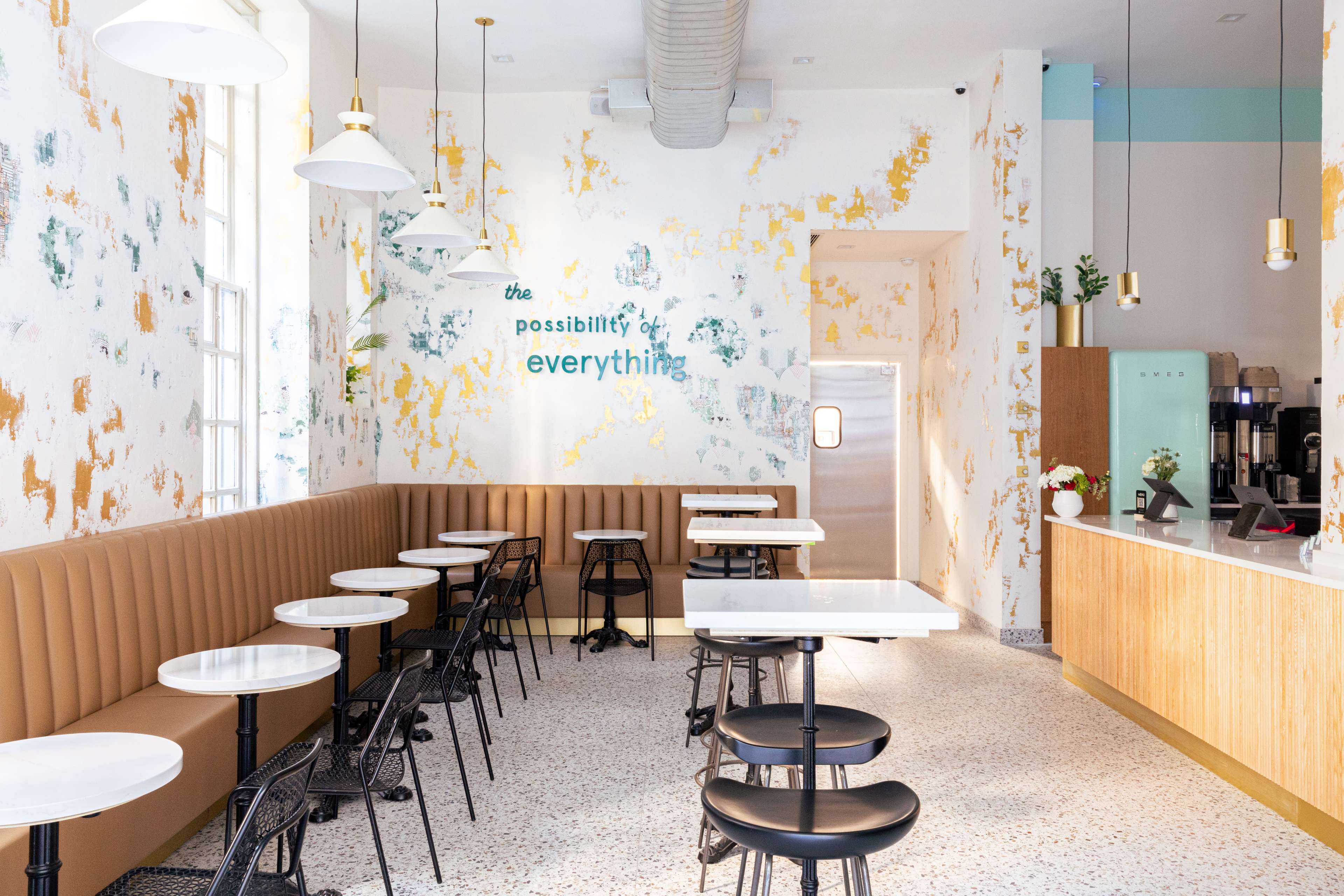 A modern café interior with a combination of wooden and metal seating, bright walls featuring a colorful texture, and a counter area at the far end.