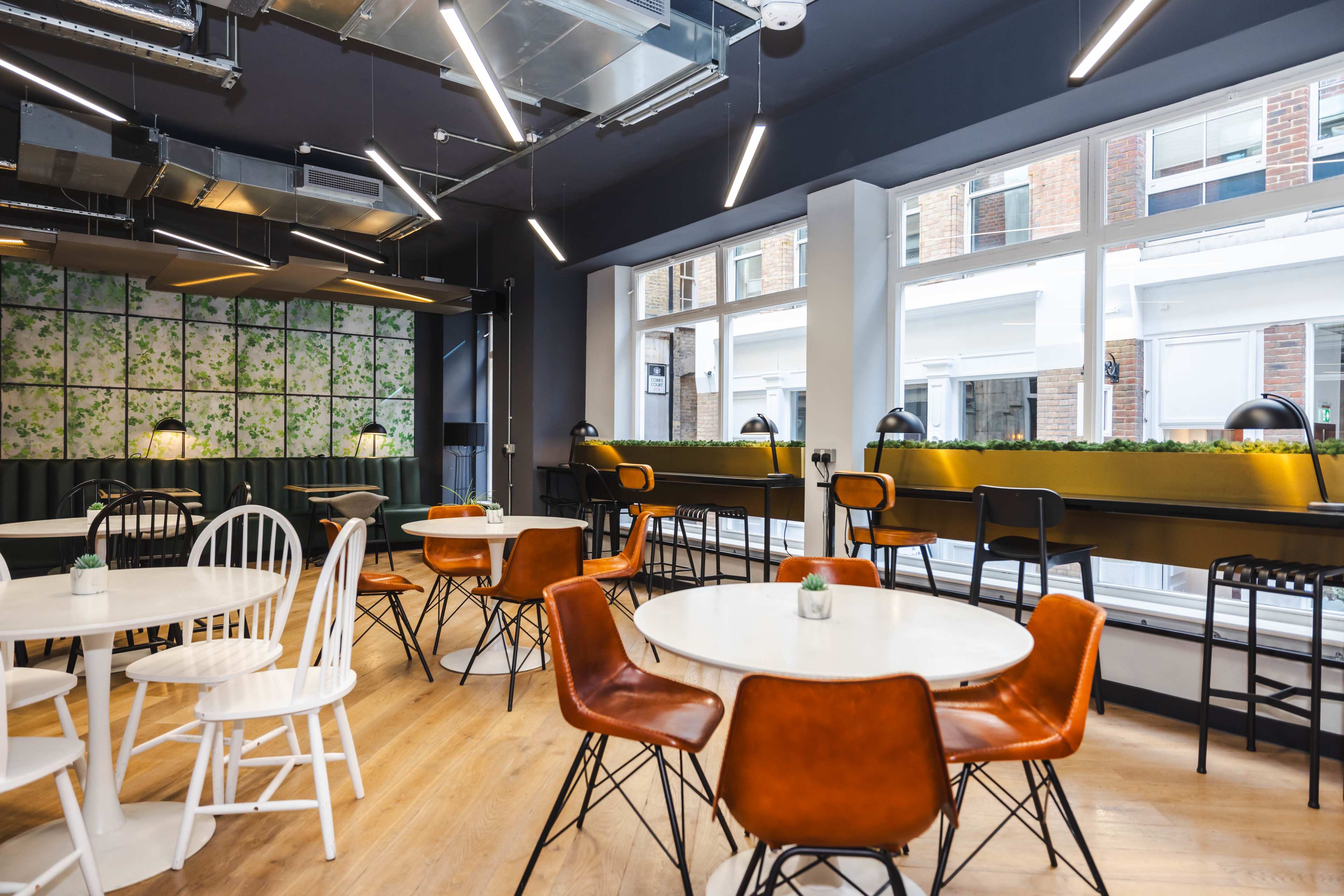 A modern café with a mix of white and brown chairs, round tables, and large windows letting in natural light.