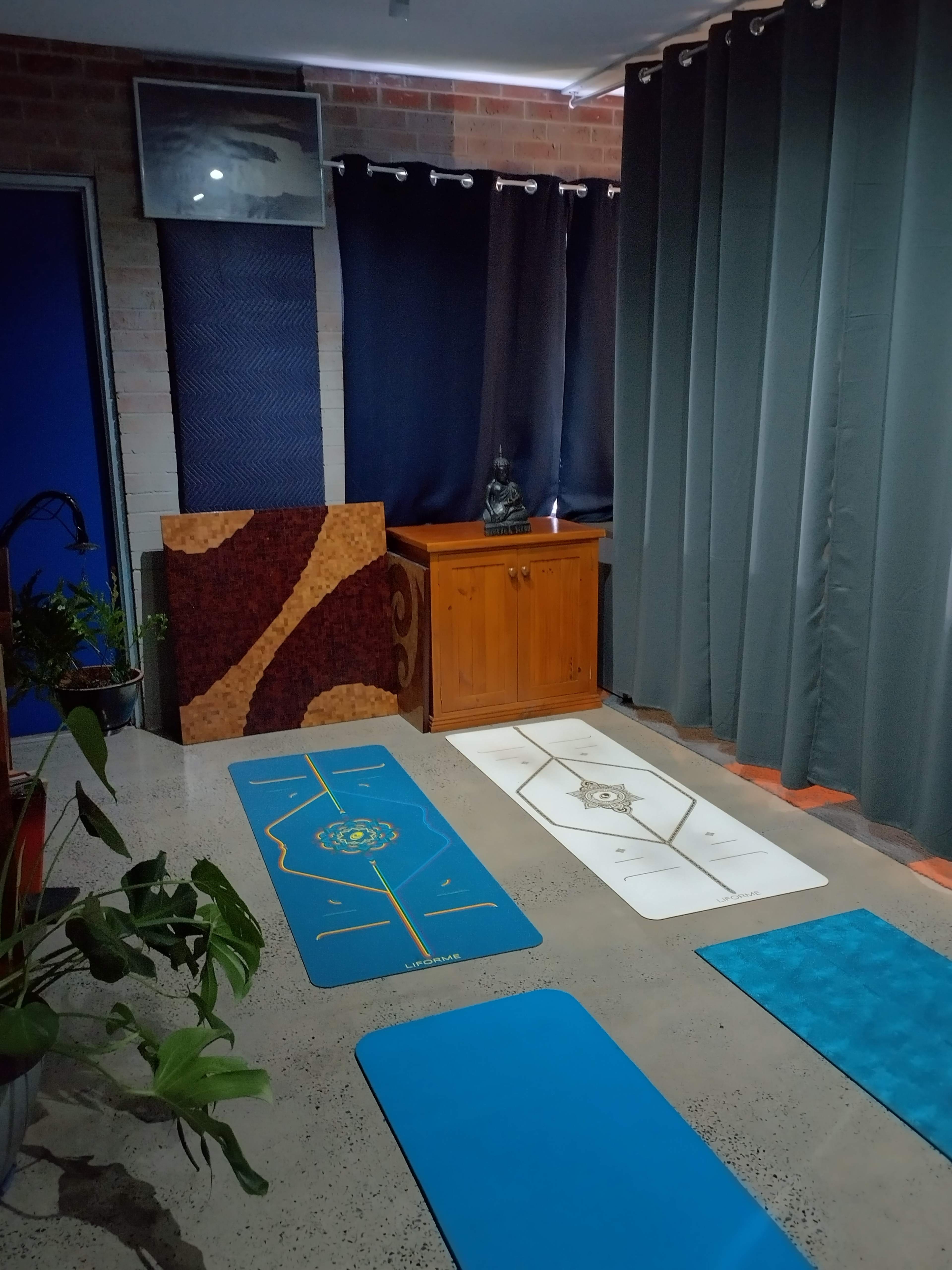 A yoga space featuring several exercise mats arranged on a polished concrete floor, with a wooden cabinet and a statue in the background, framed by dark curtains.