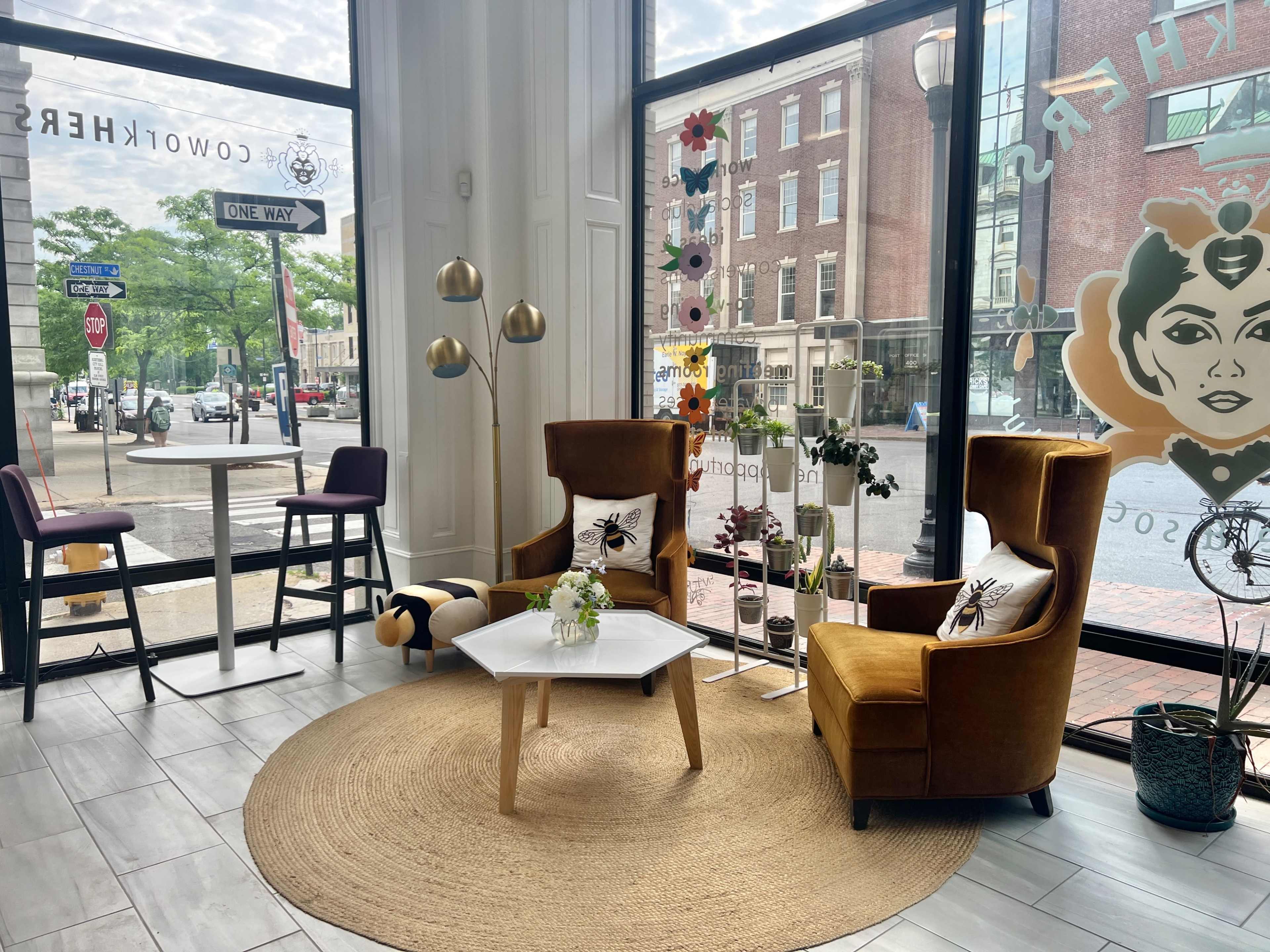 A cozy seating area with two plush armchairs, a small table, and a round rug, all positioned next to a large window overlooking a street with traffic signs.