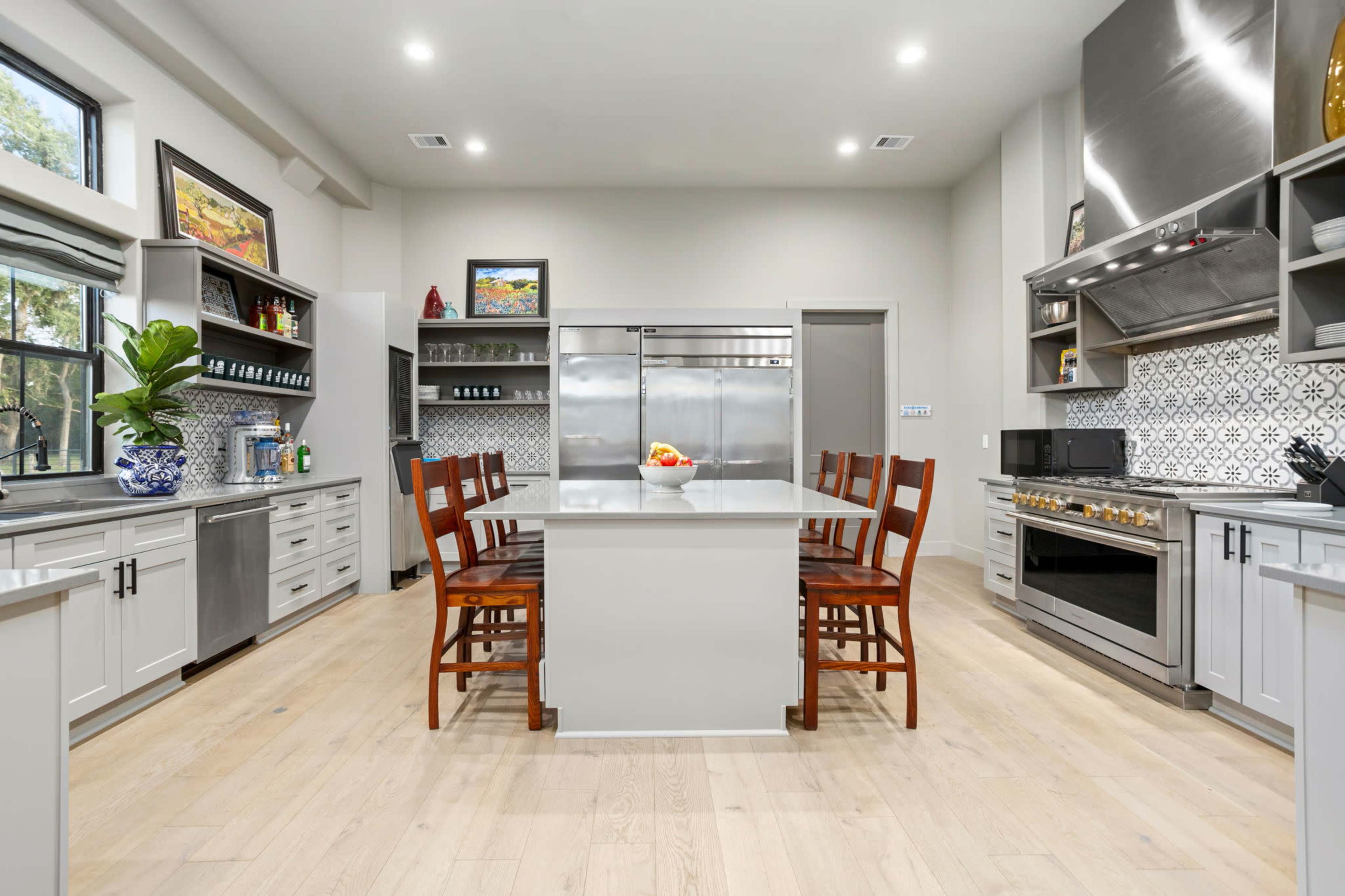A modern kitchen features an island with seating, stainless steel appliances, and light-colored cabinetry arranged around a tile backsplash.