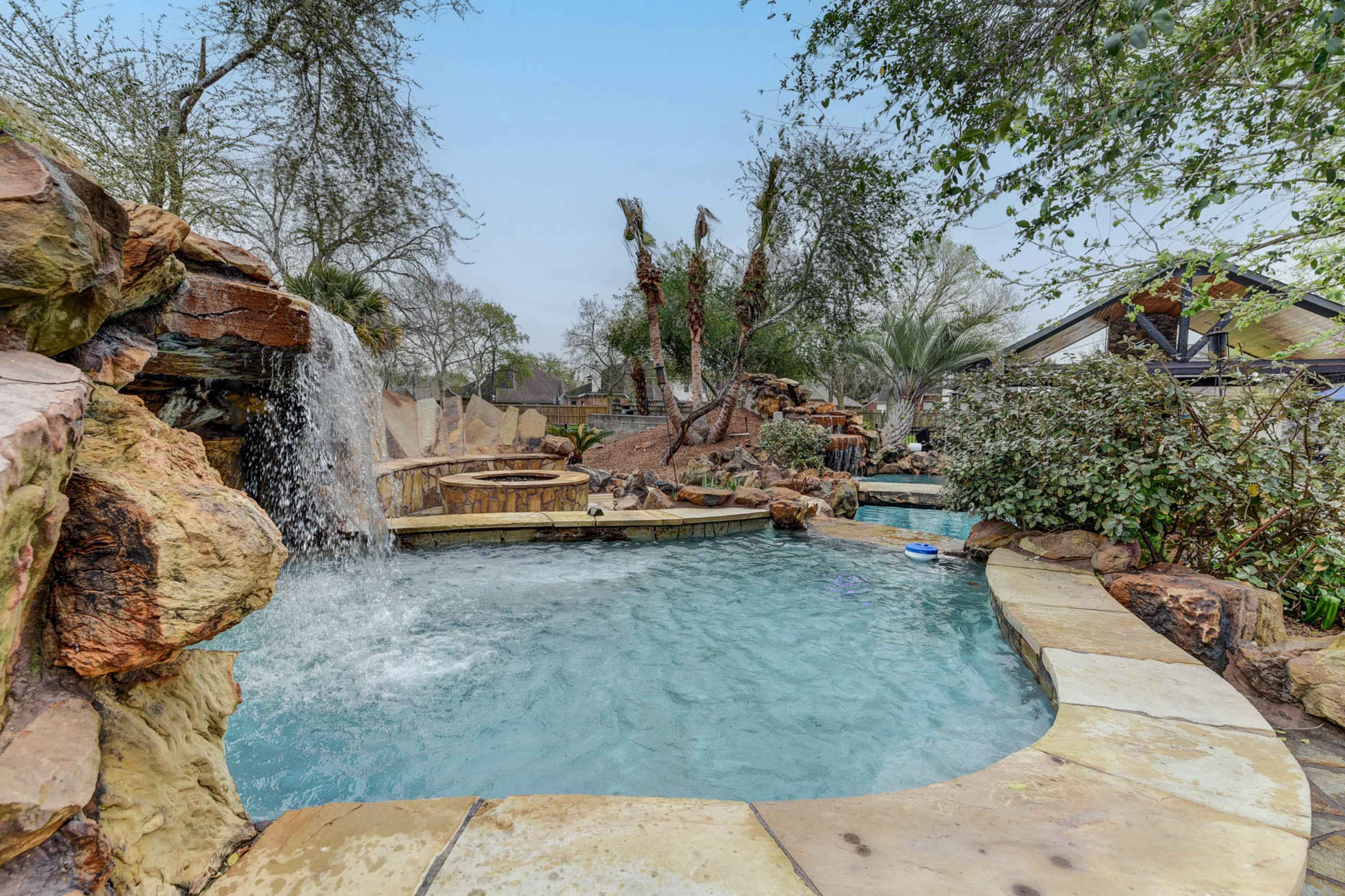 The scene features a landscaped pool area with rock formations, a waterfall, and surrounding greenery.