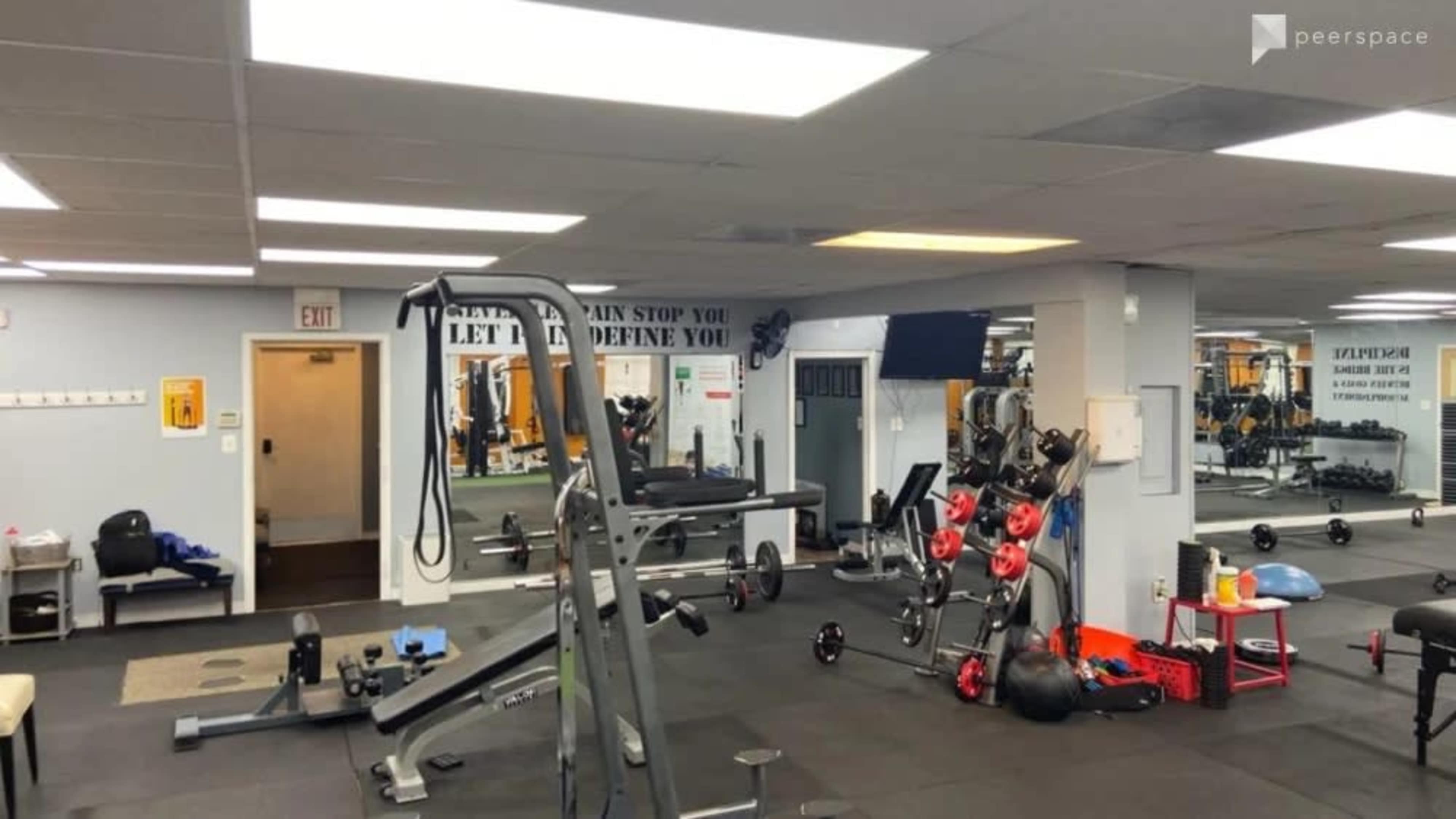 A gym interior with various exercise equipment, including weights and a bench, and motivational quotes on the walls.