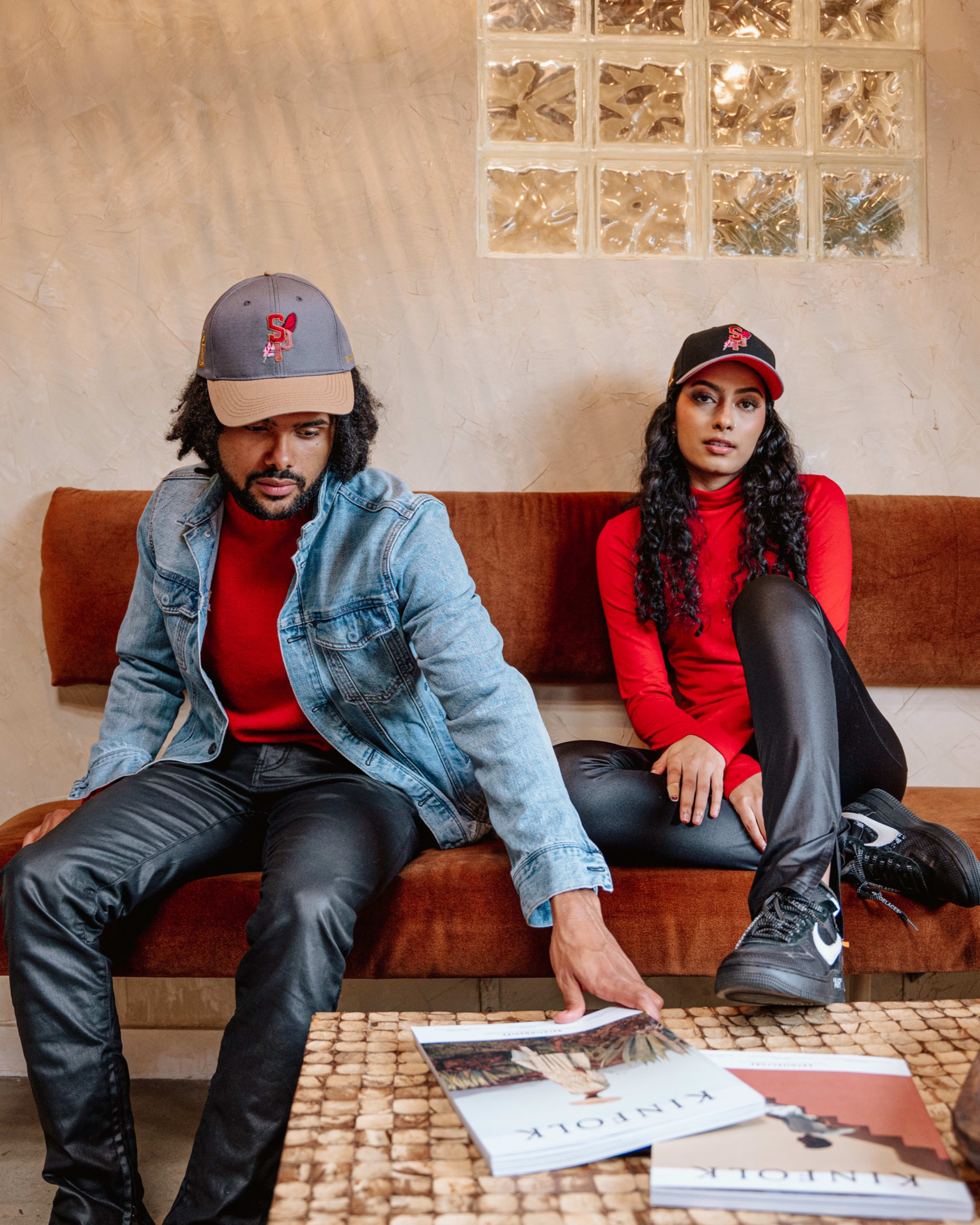 A fashion photo shoot with a man and a woman sitting on an orange couch.