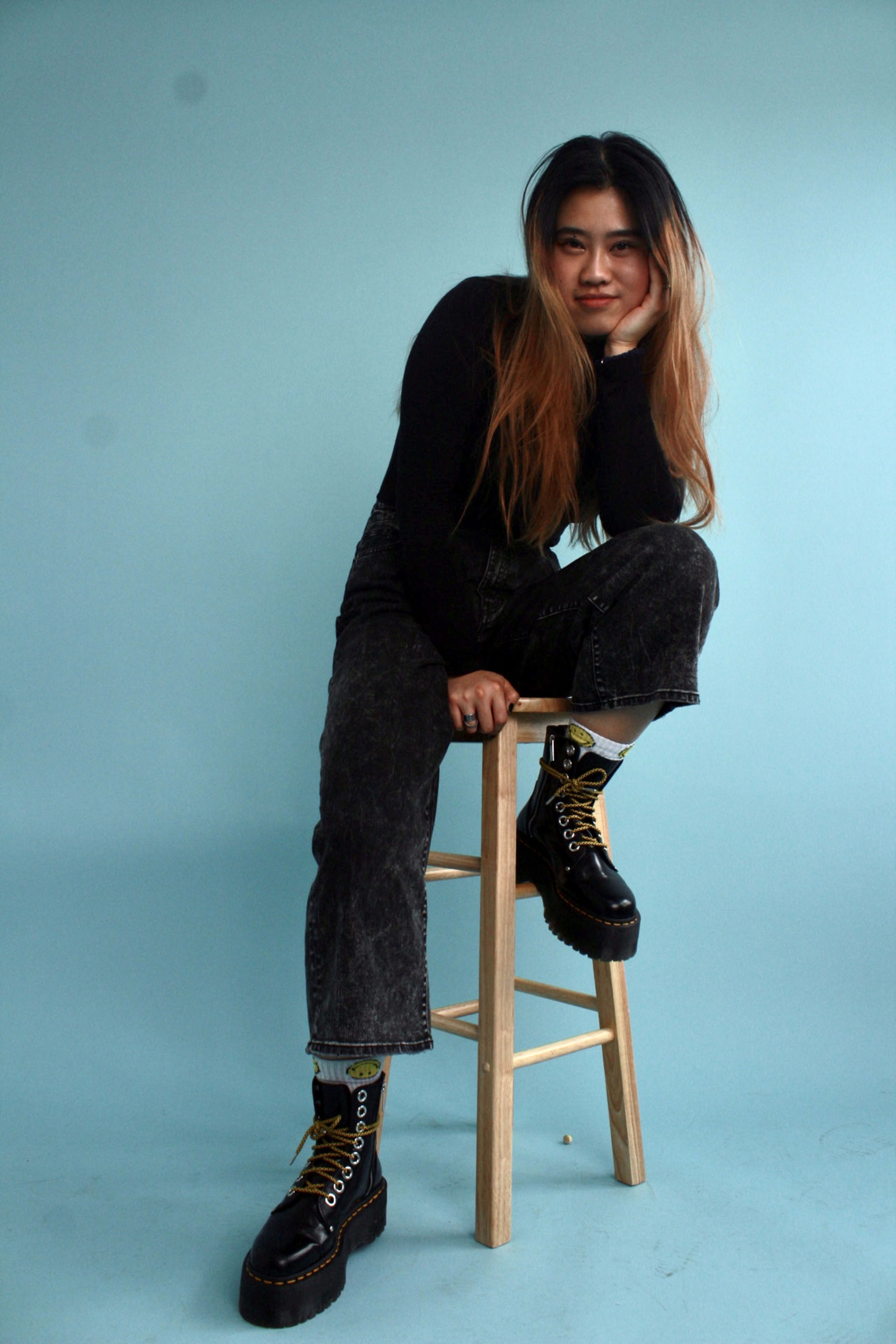 A woman sitting on a wooden stool for a photoshoot.