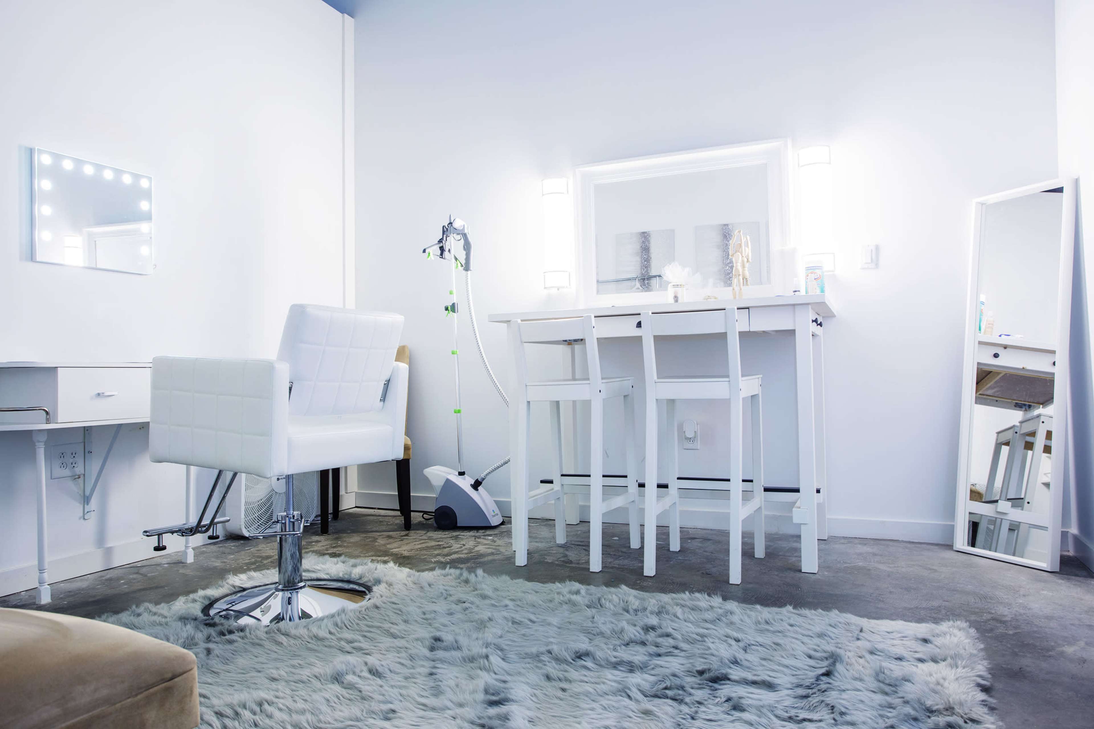 The image shows a modern beauty salon interior with a white vanity table, two chairs, and a full-length mirror on a light gray carpet.
