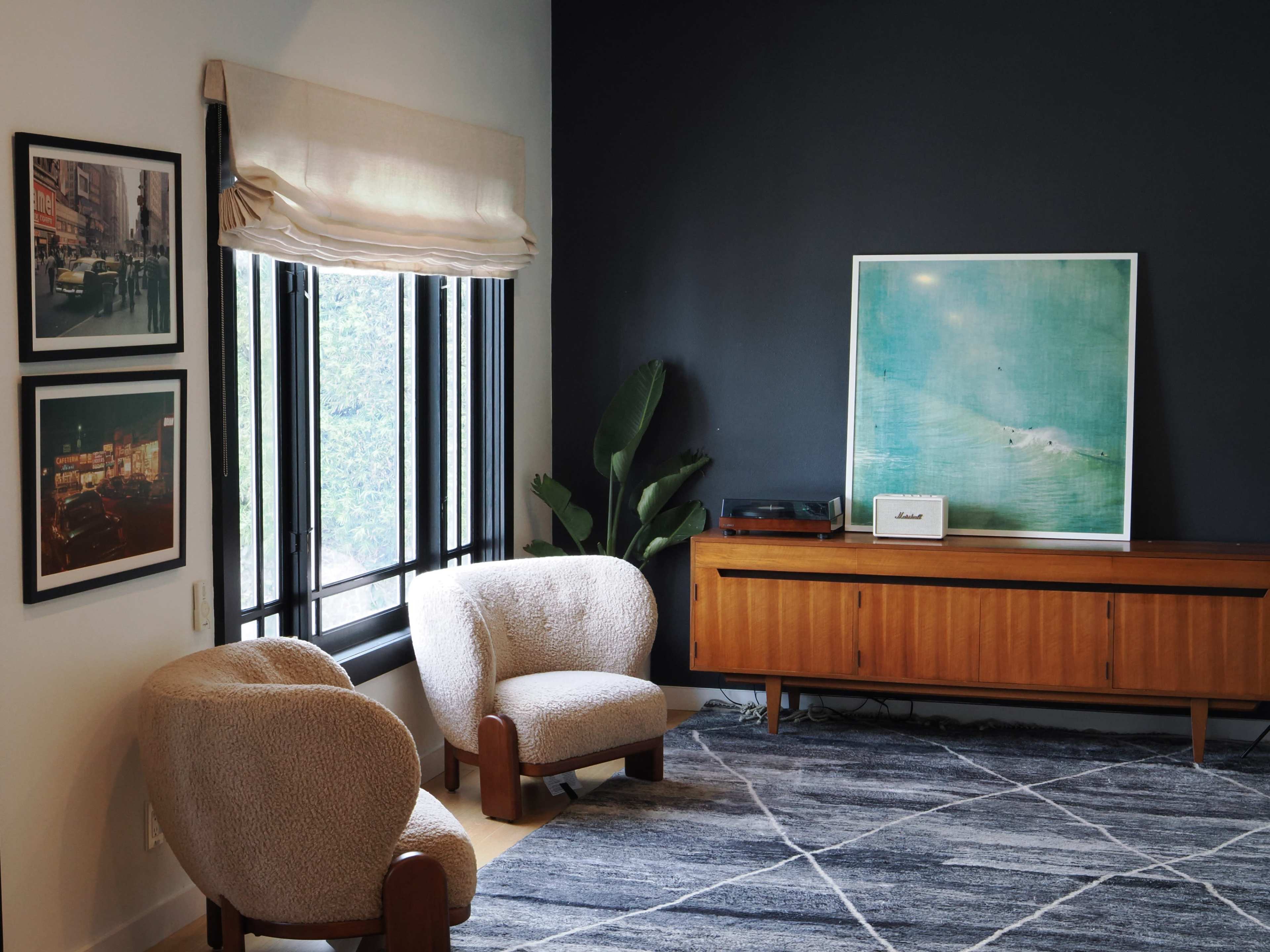 A cozy living room features two upholstered chairs, a wooden sideboard, framed photographs on the wall, and a large artwork above the sideboard.