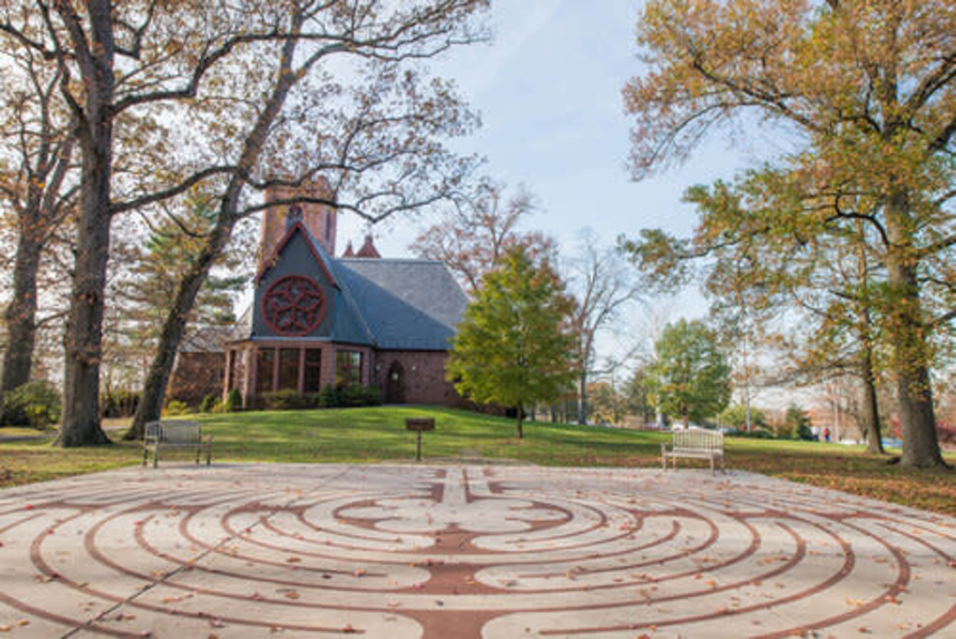 A stone labyrinth is set in a park in front of a brick church surrounded by trees.