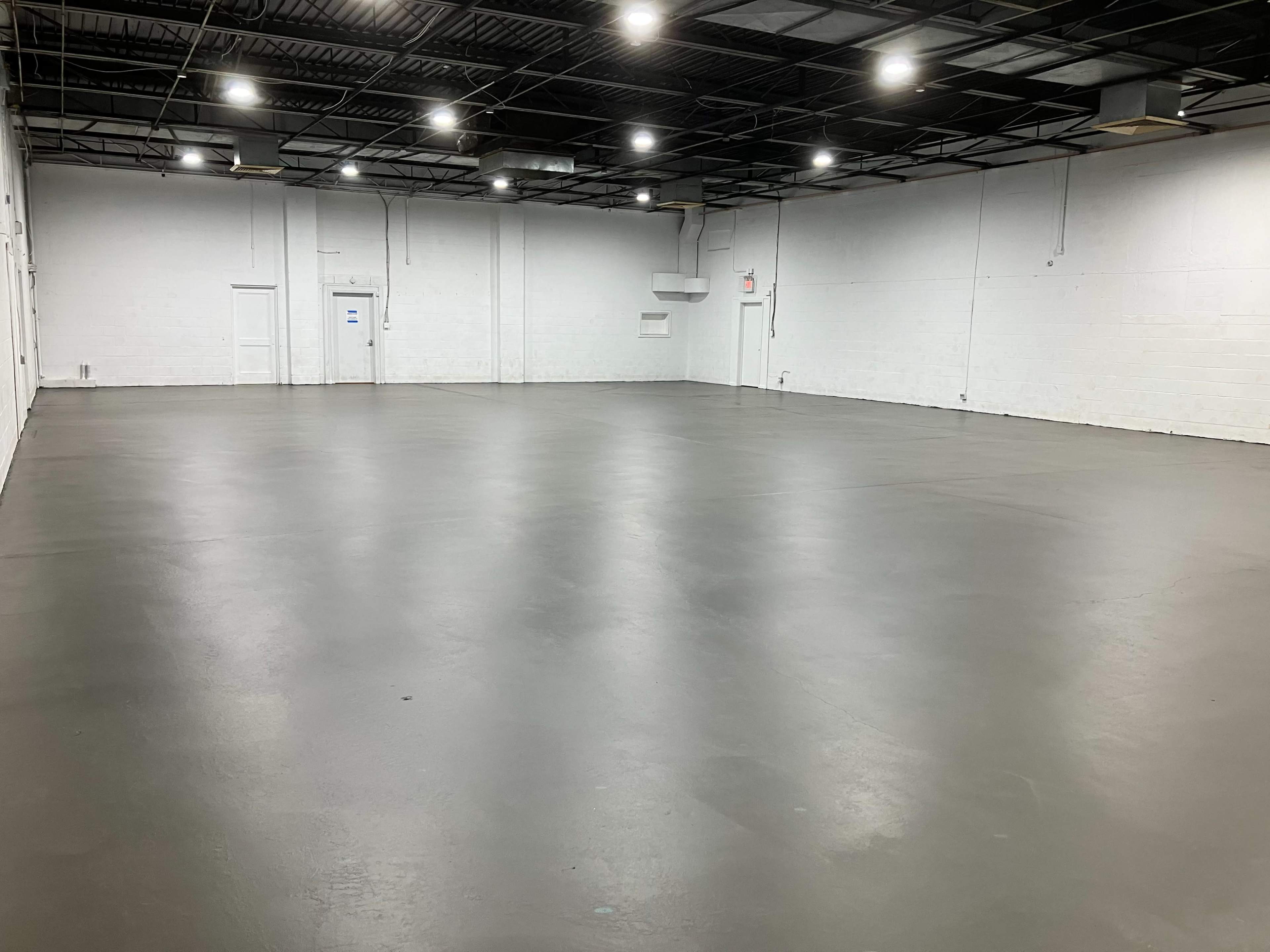 An empty, spacious room with a concrete floor and overhead lighting.