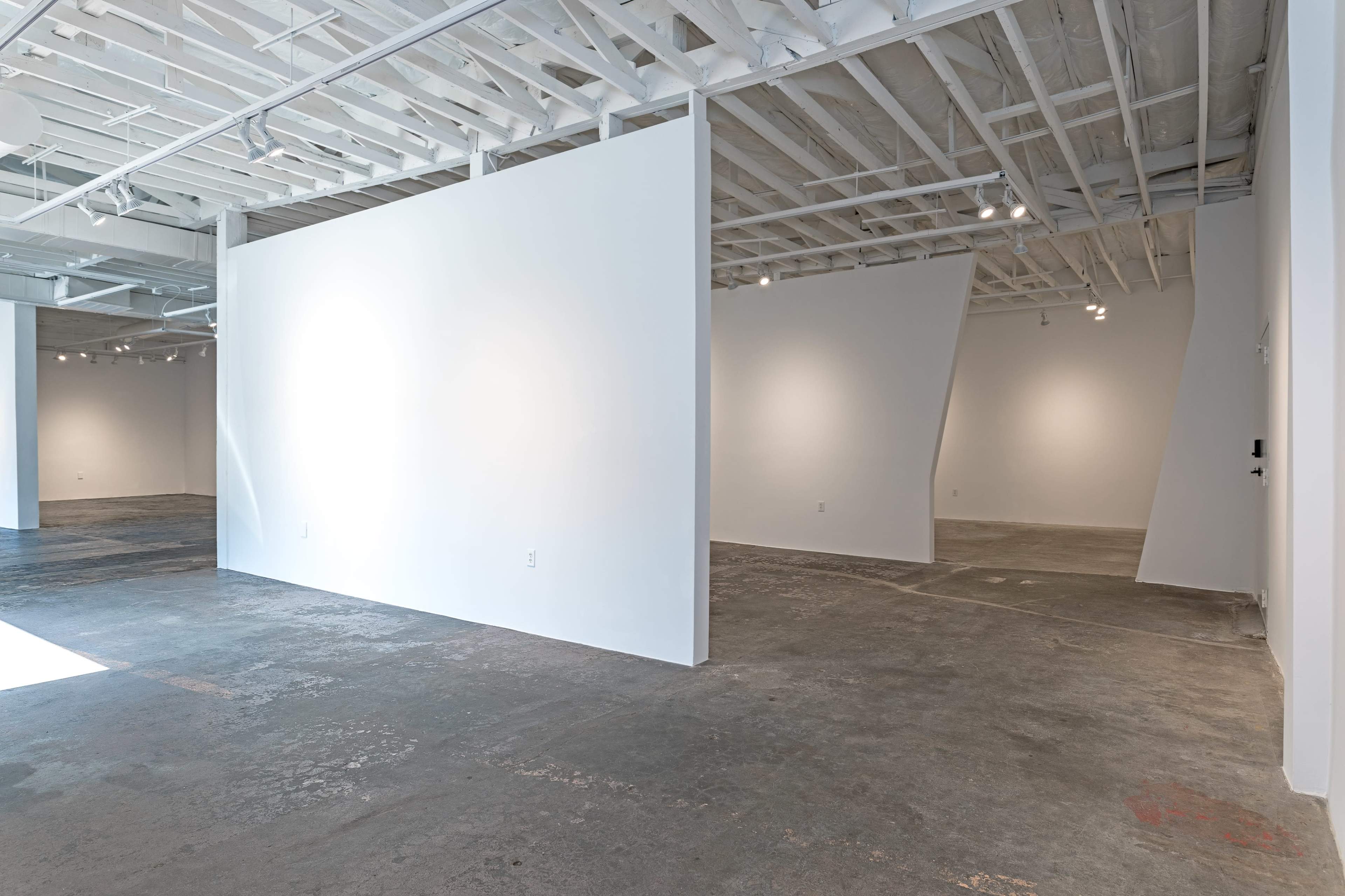 A minimalist art gallery features white walls and a concrete floor, with varying angles and lighting throughout the space.