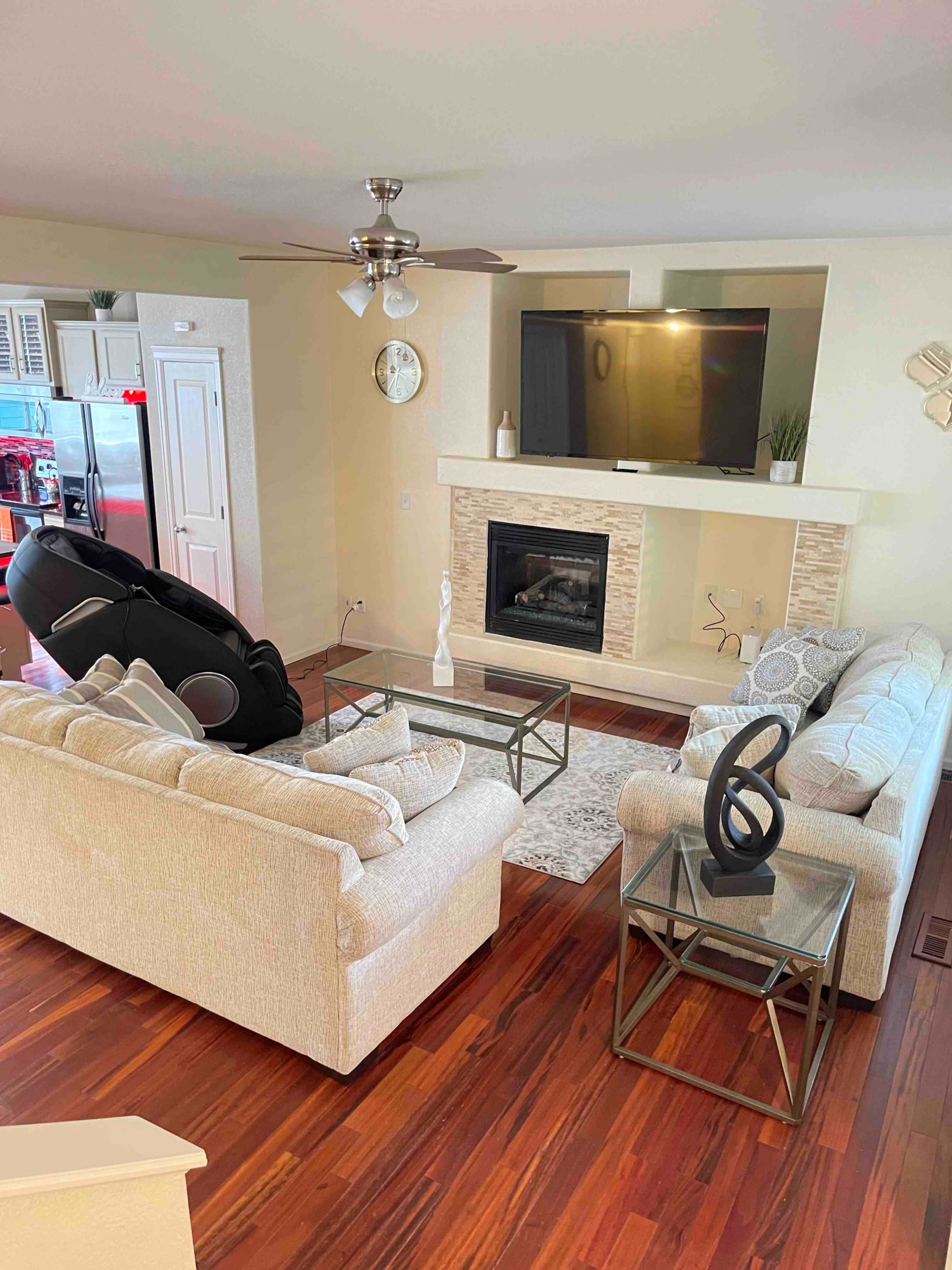 The image shows a living room with a beige sofa set, a glass coffee table, and a fireplace, complemented by a television mounted on the wall.