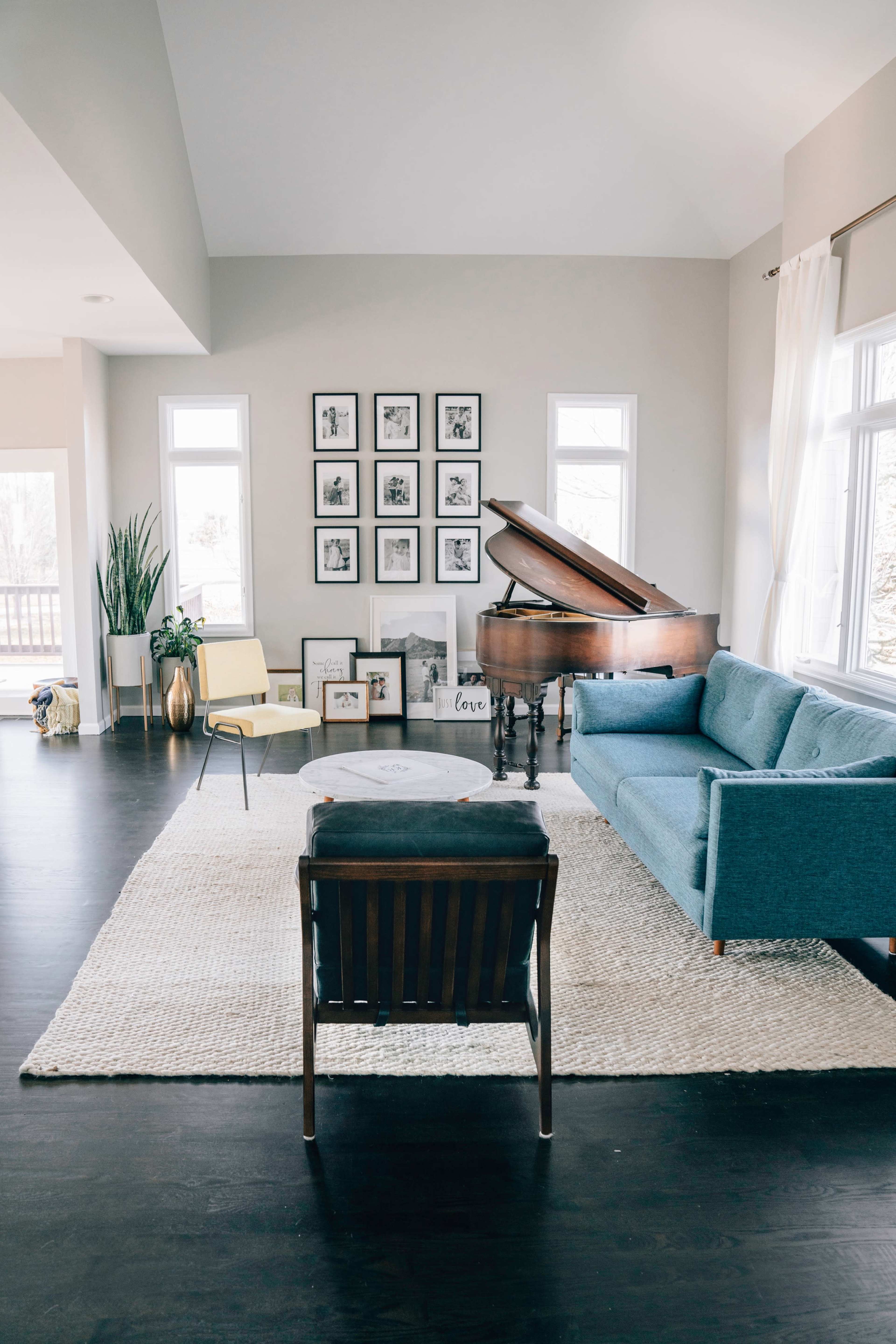 A spacious living room features a grand piano, a blue sofa, a coffee table, and a wall adorned with framed photos.