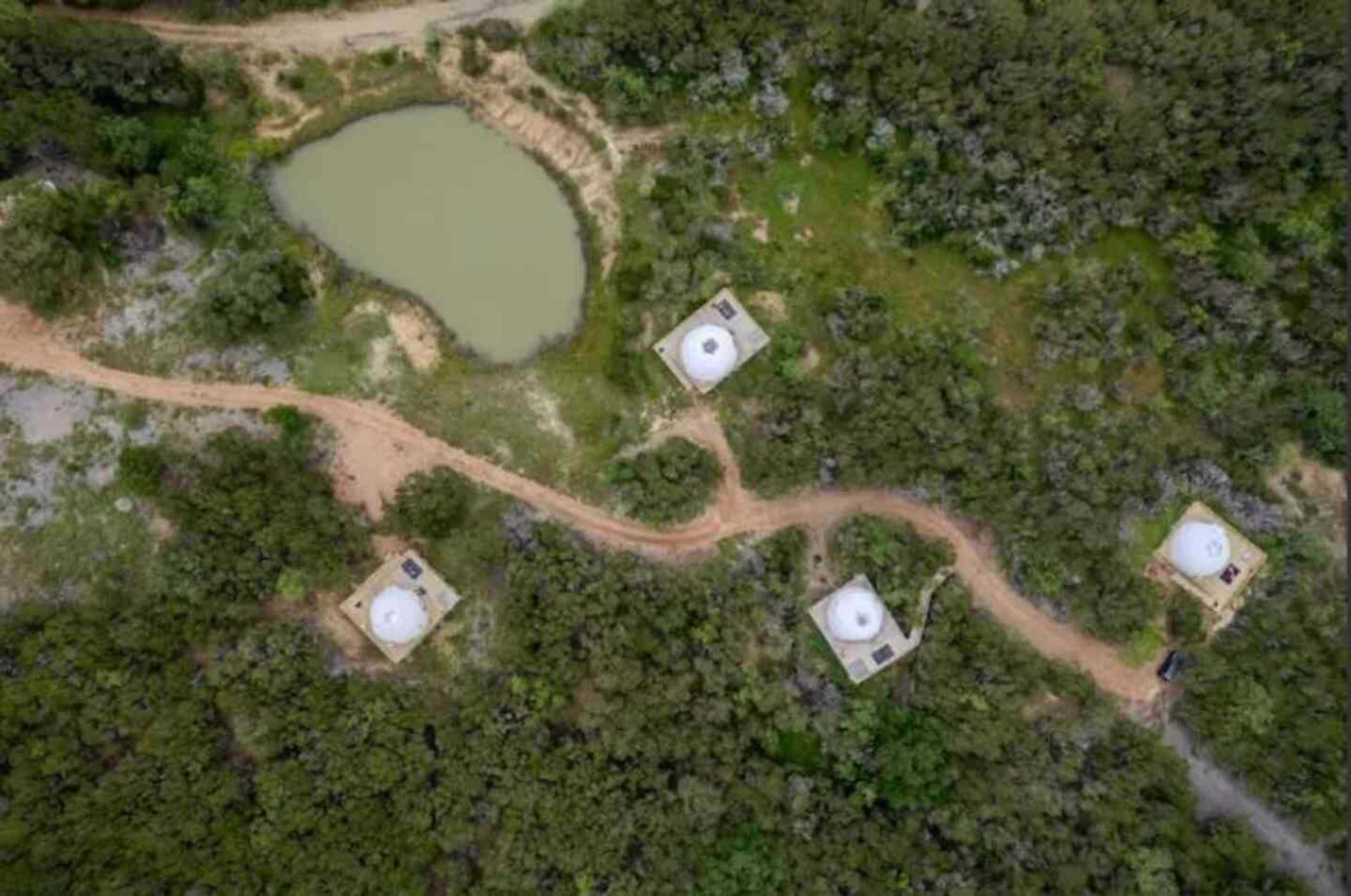 The image shows an aerial view of several dome-shaped structures situated near a small pond and surrounded by dense vegetation.