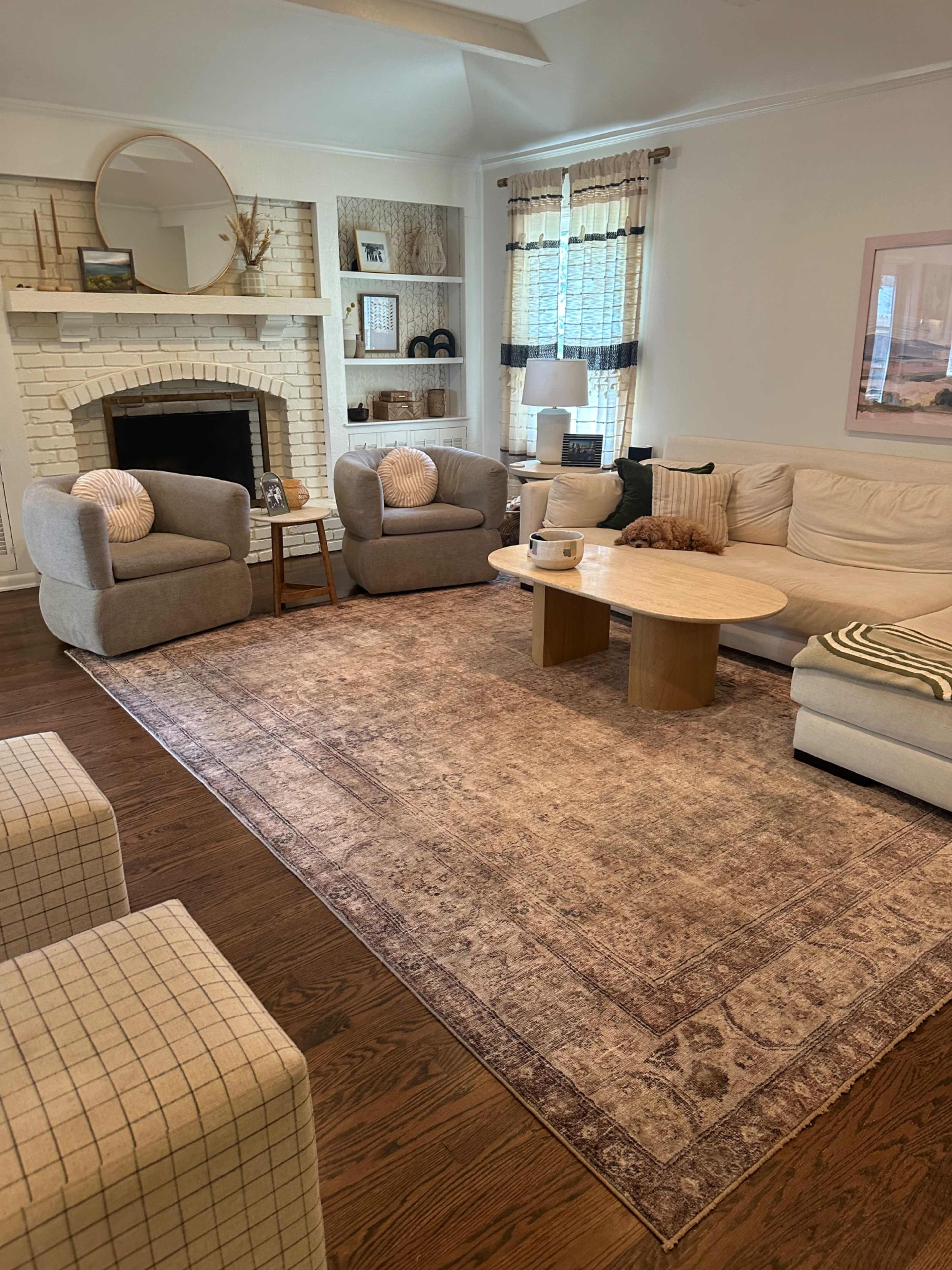 The living room features a light-colored sectional sofa, two armchairs, a round coffee table, and a fireplace with decorative items on the mantel.