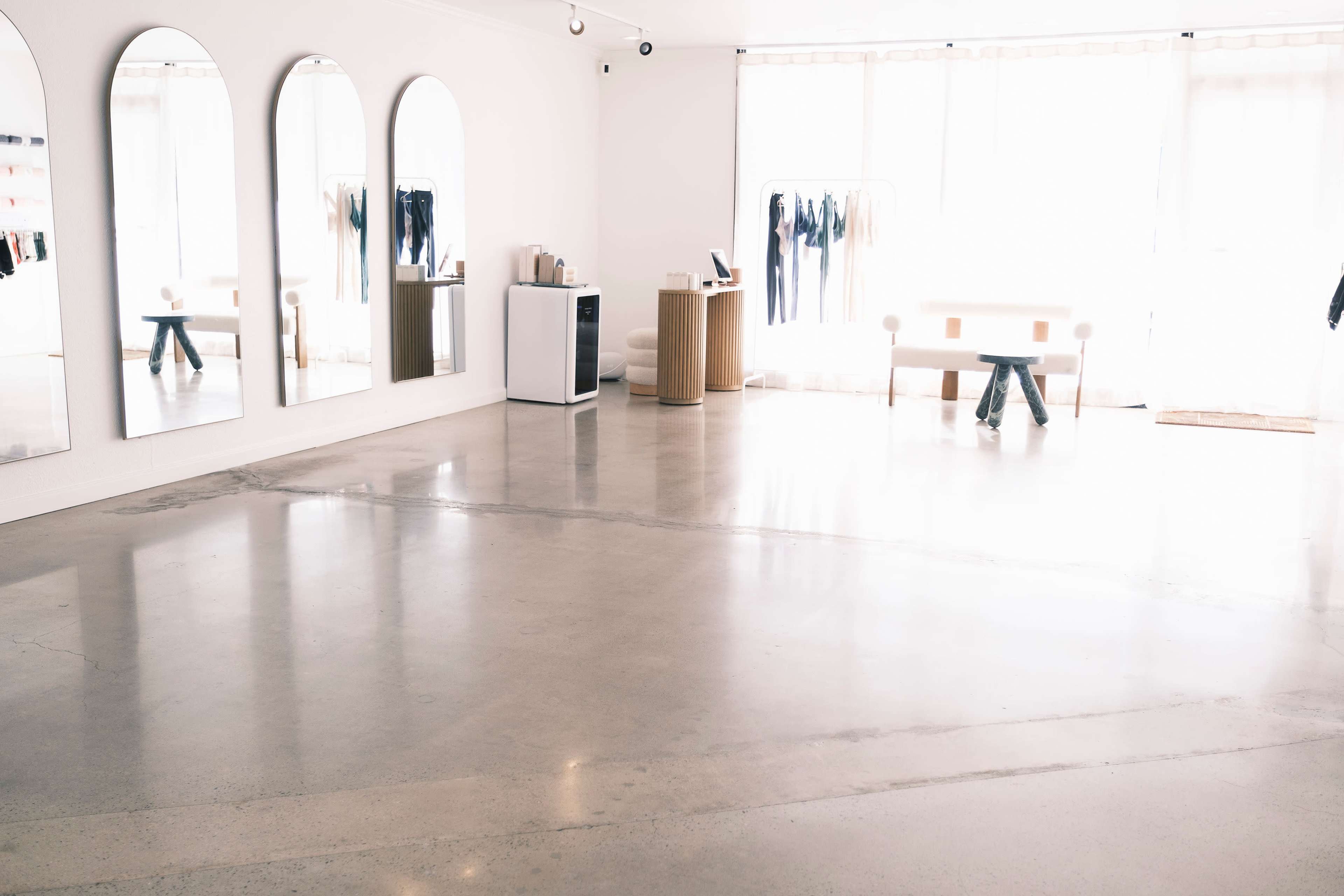 A minimalist room with three arched mirrors, a small table, a clothing rack, and polished concrete flooring.