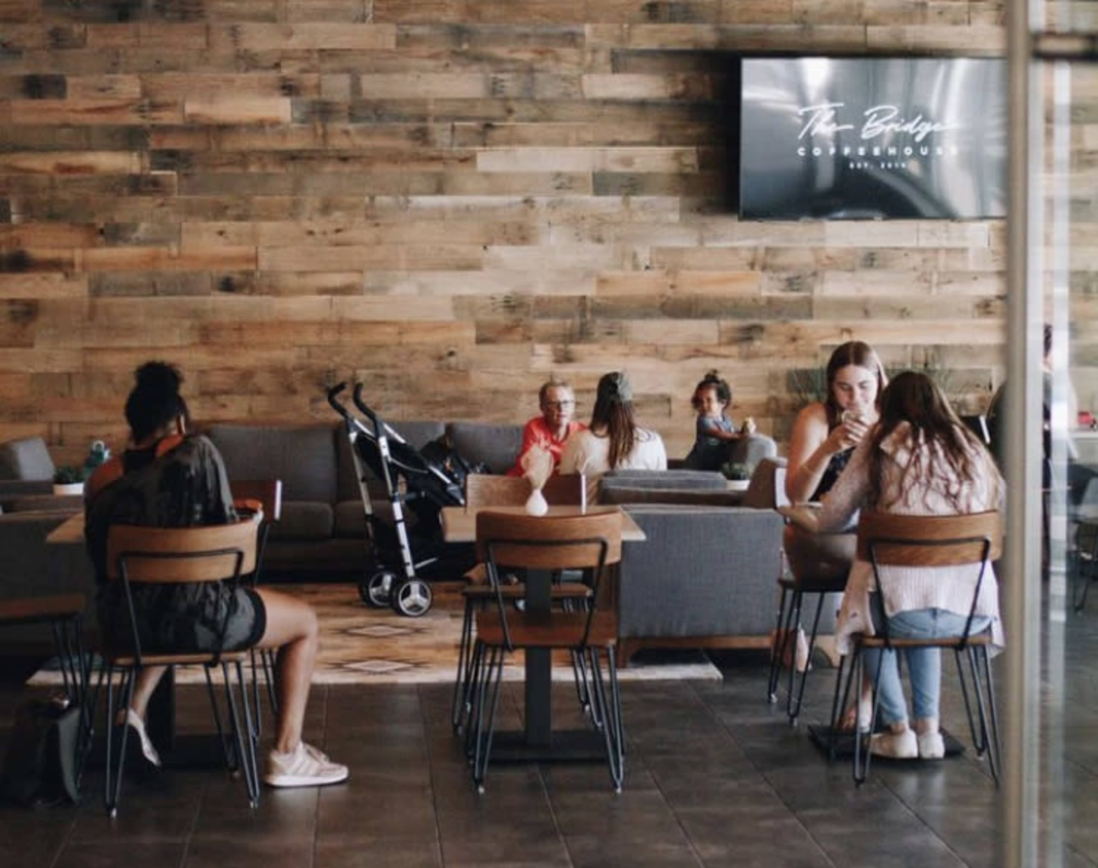 A modern coffee shop with wooden walls, where several people are seated at tables, some working on laptops, while a stroller is visible nearby.