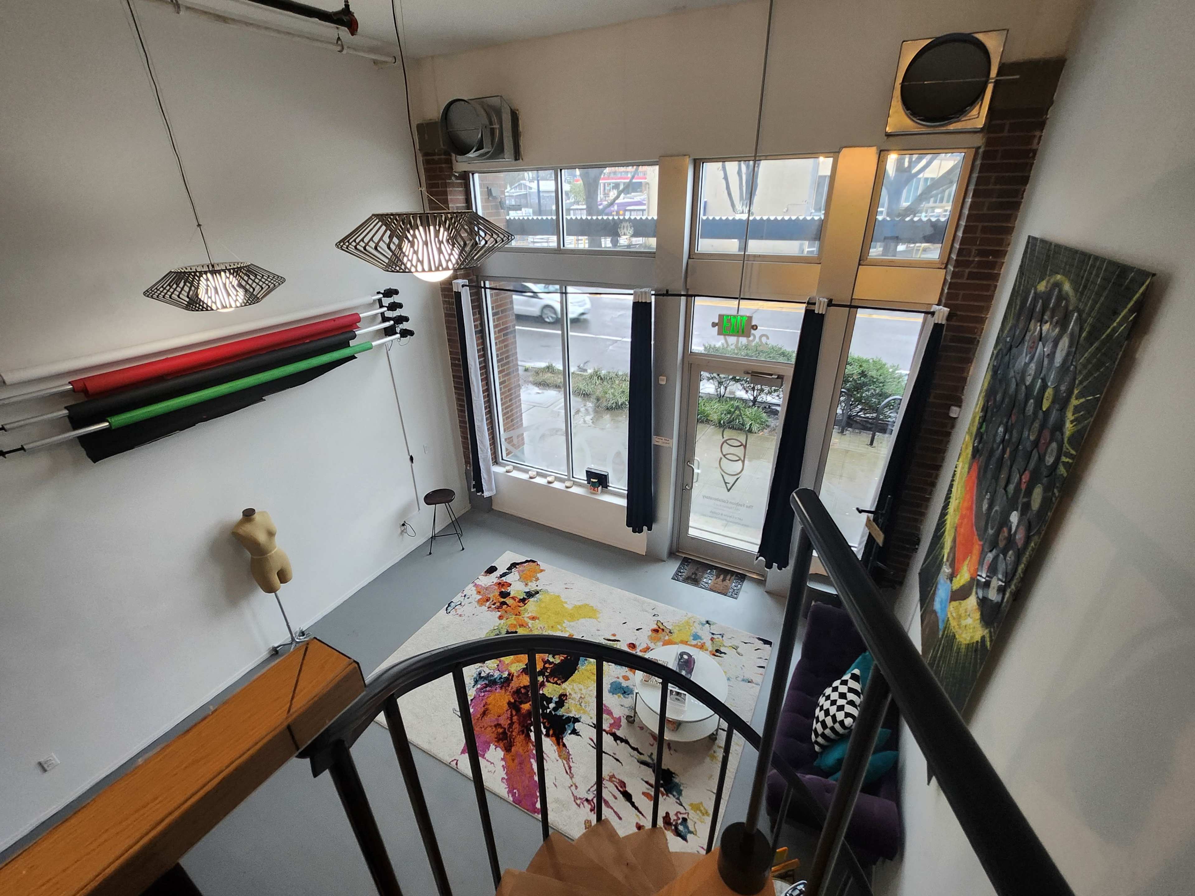 A spacious interior from an elevated viewpoint, featuring a spiral staircase, colorful artwork, and large windows facing the street.