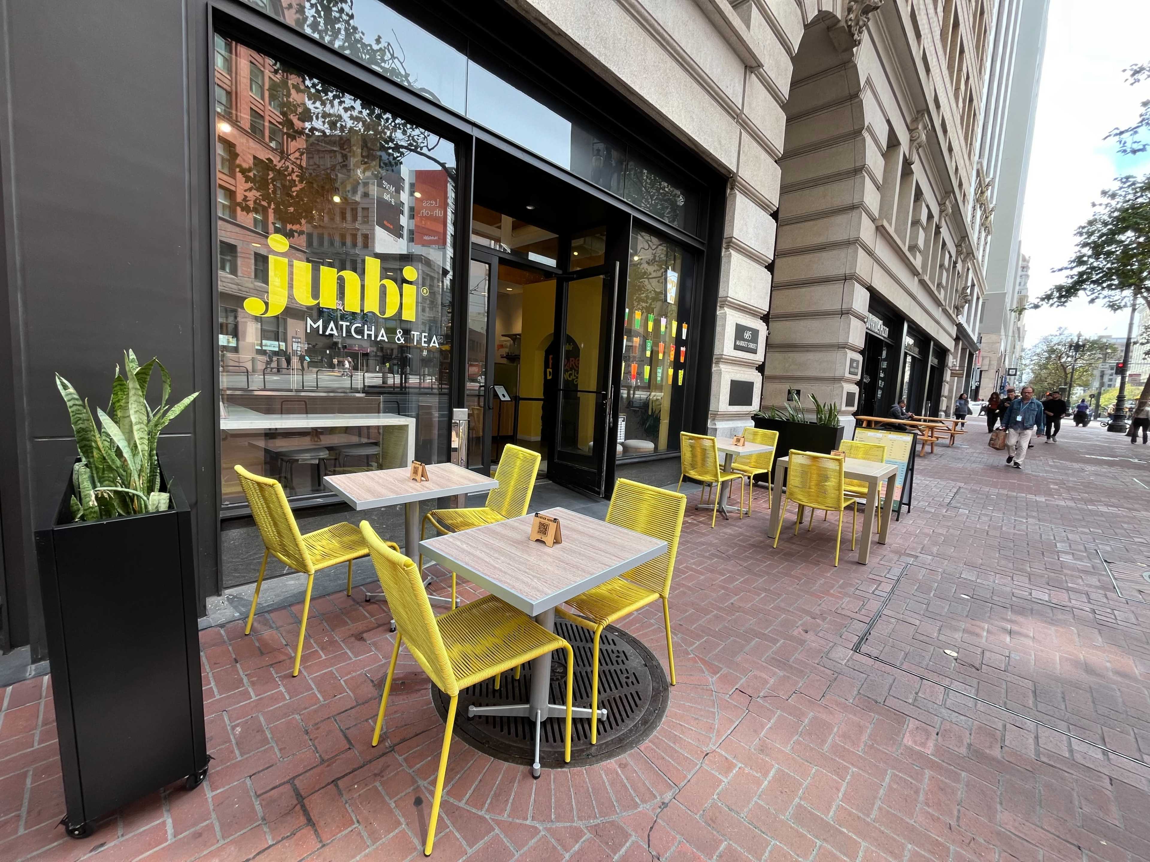The image shows an outdoor seating area with yellow chairs and tables in front of a matcha tea shop named "junbi."