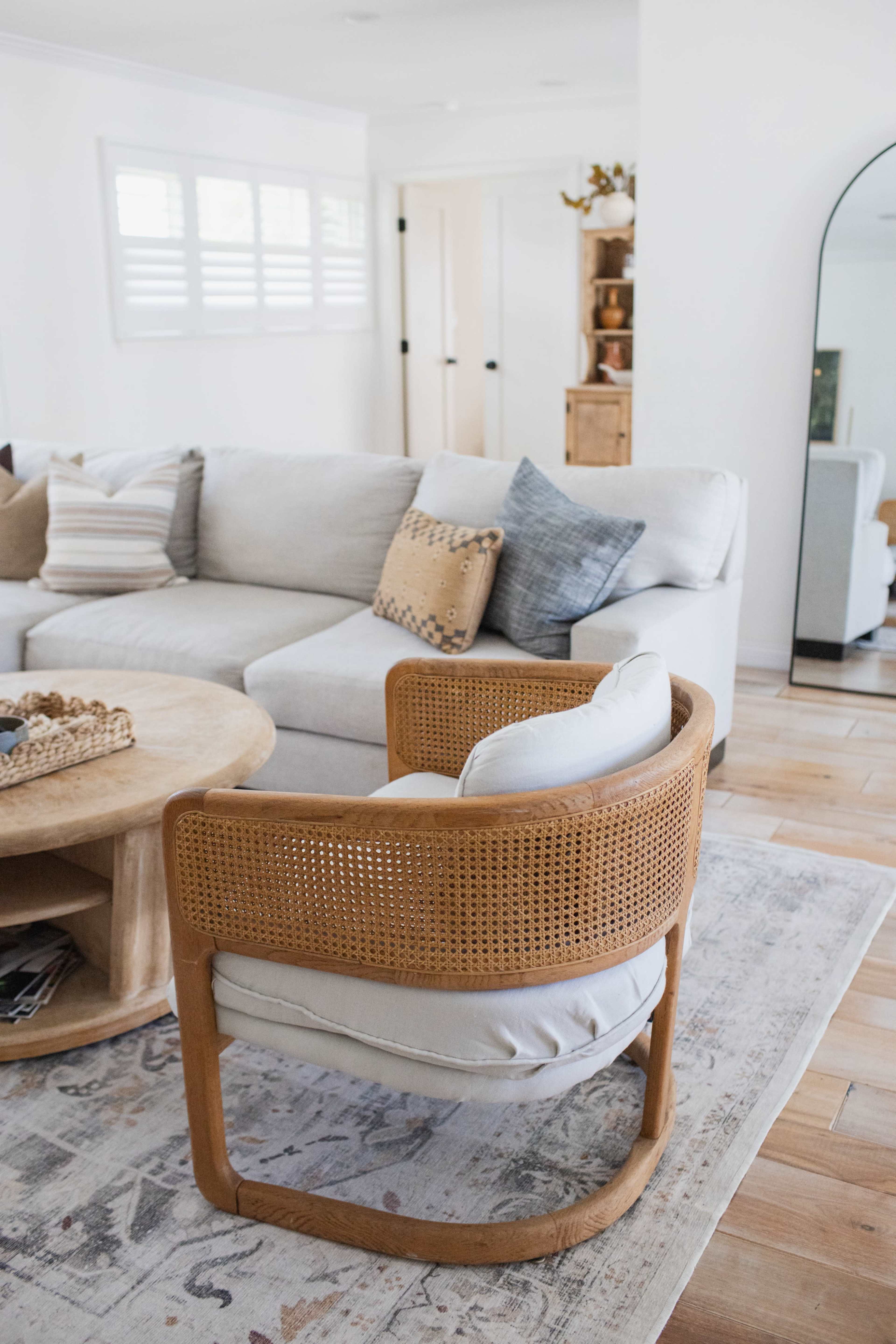 A comfortable living room features a light-colored sectional sofa, a round coffee table, and a rattan accent chair on a patterned rug.