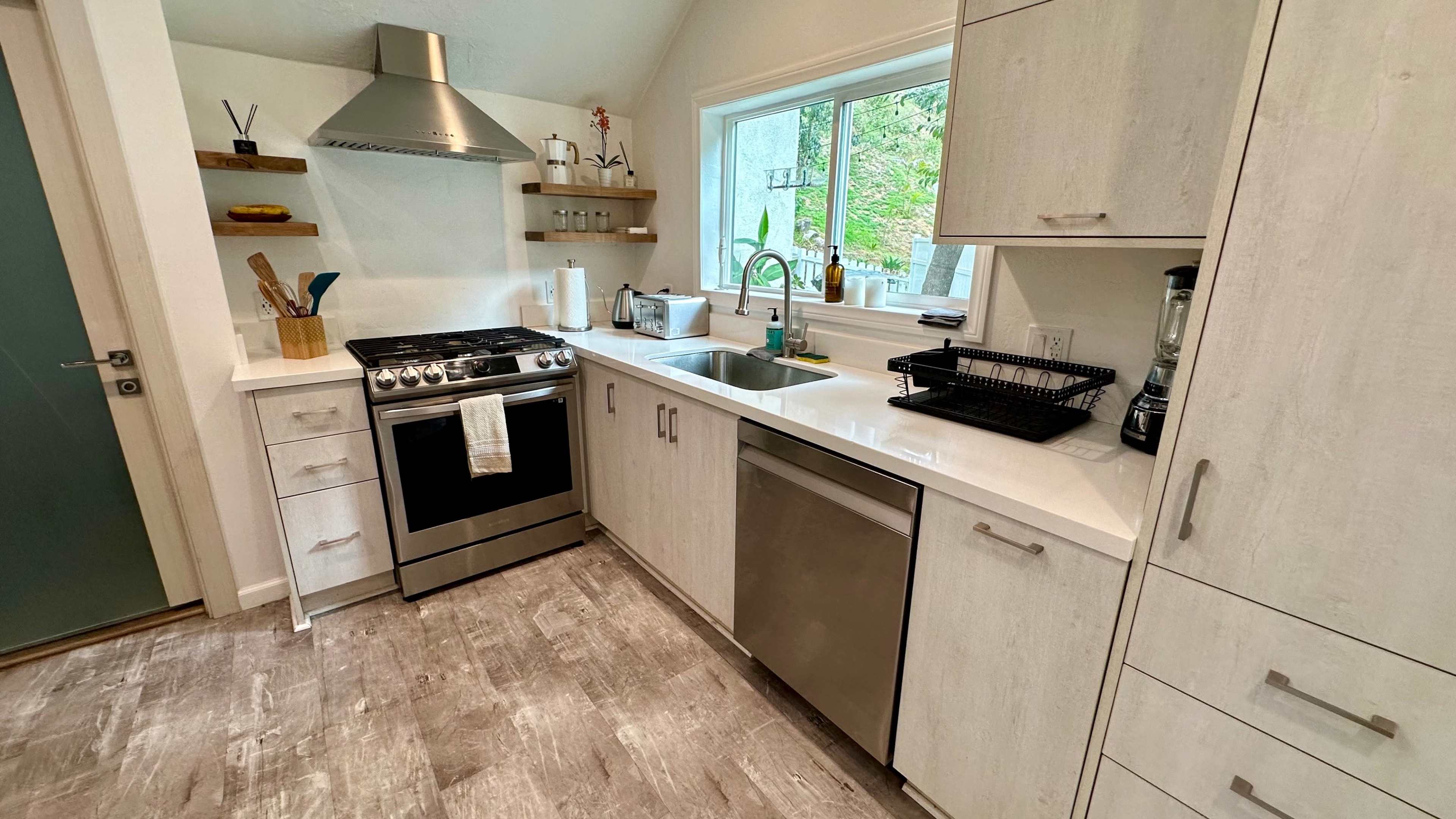 A modern kitchen with stainless steel appliances, white cabinetry, and a sink located beside a window.