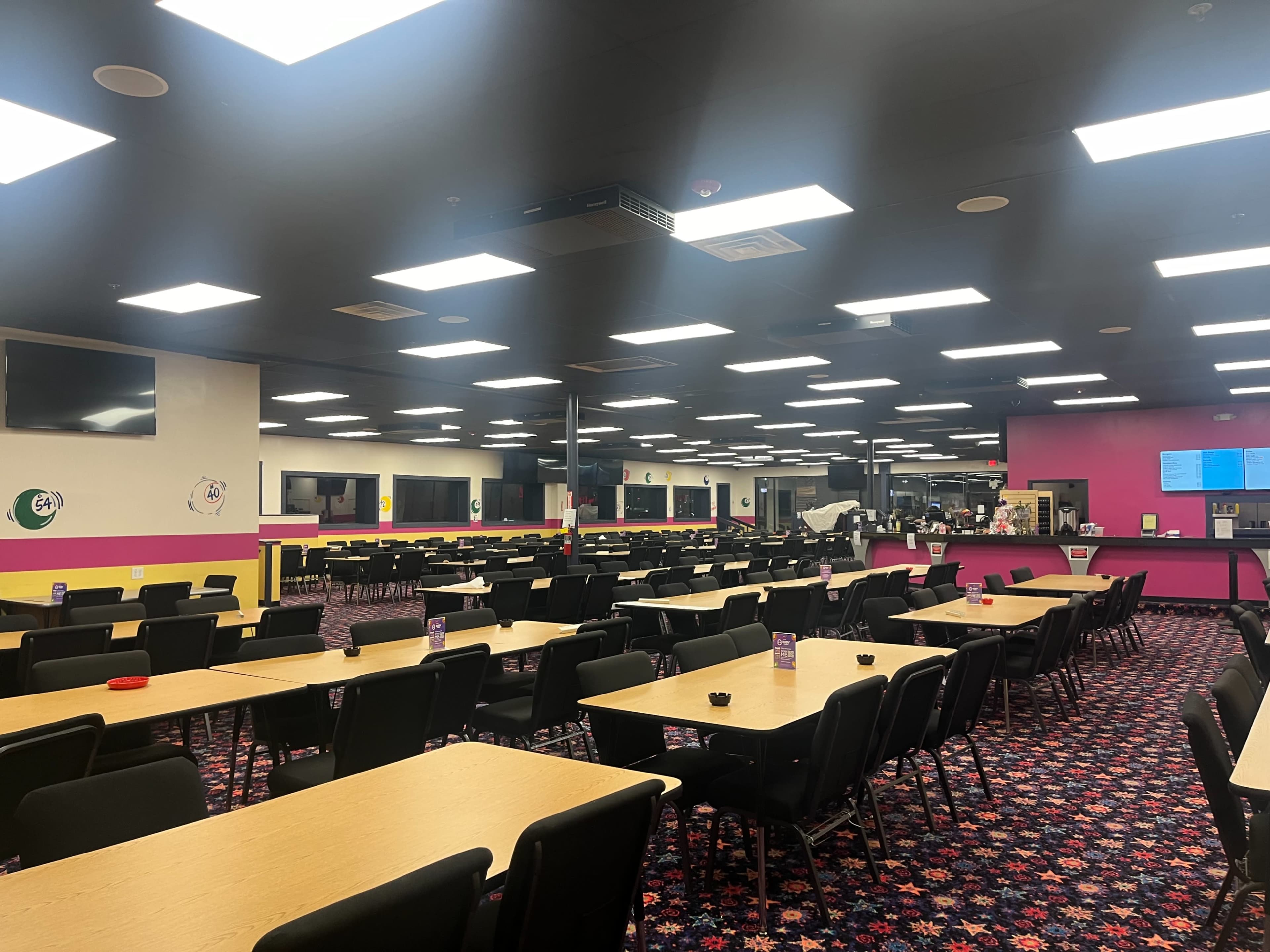 An empty dining area features rows of tables and chairs, with brightly colored walls and overhead lights illuminating the space.