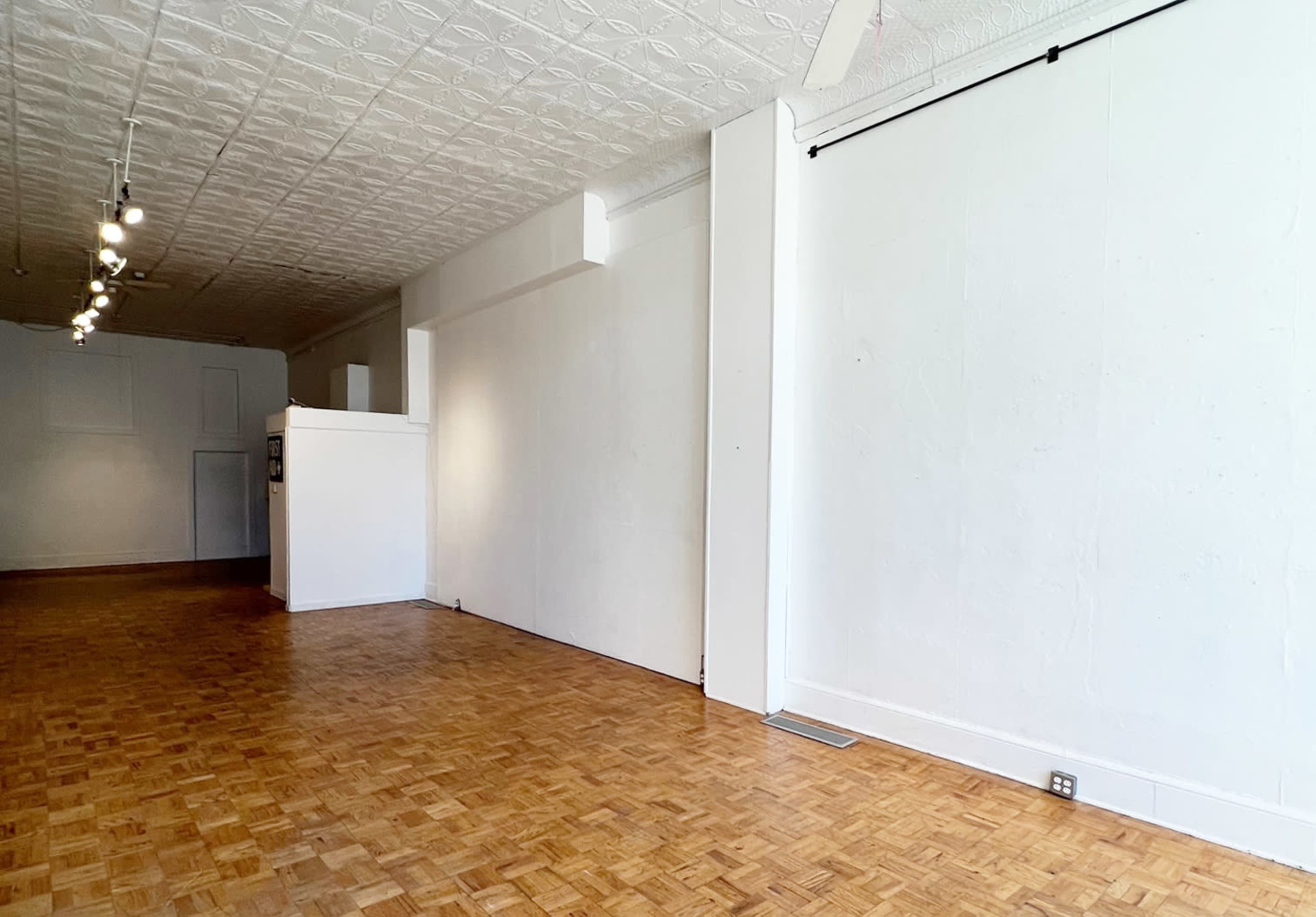 The image shows a spacious, empty interior with a wooden floor, white walls, and a ceiling featuring decorative tiles.