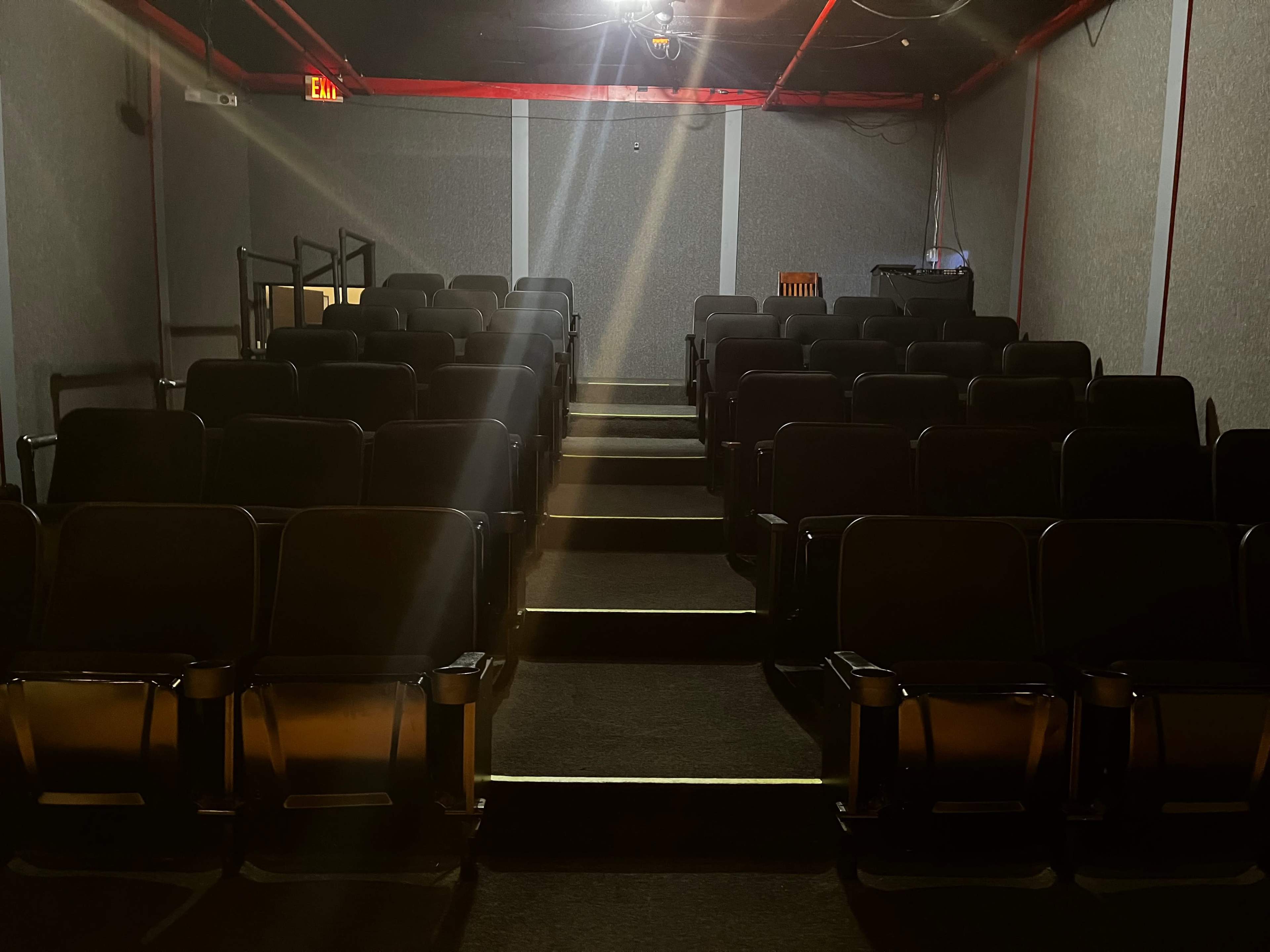 An empty movie theater with rows of black seats and dim lighting.