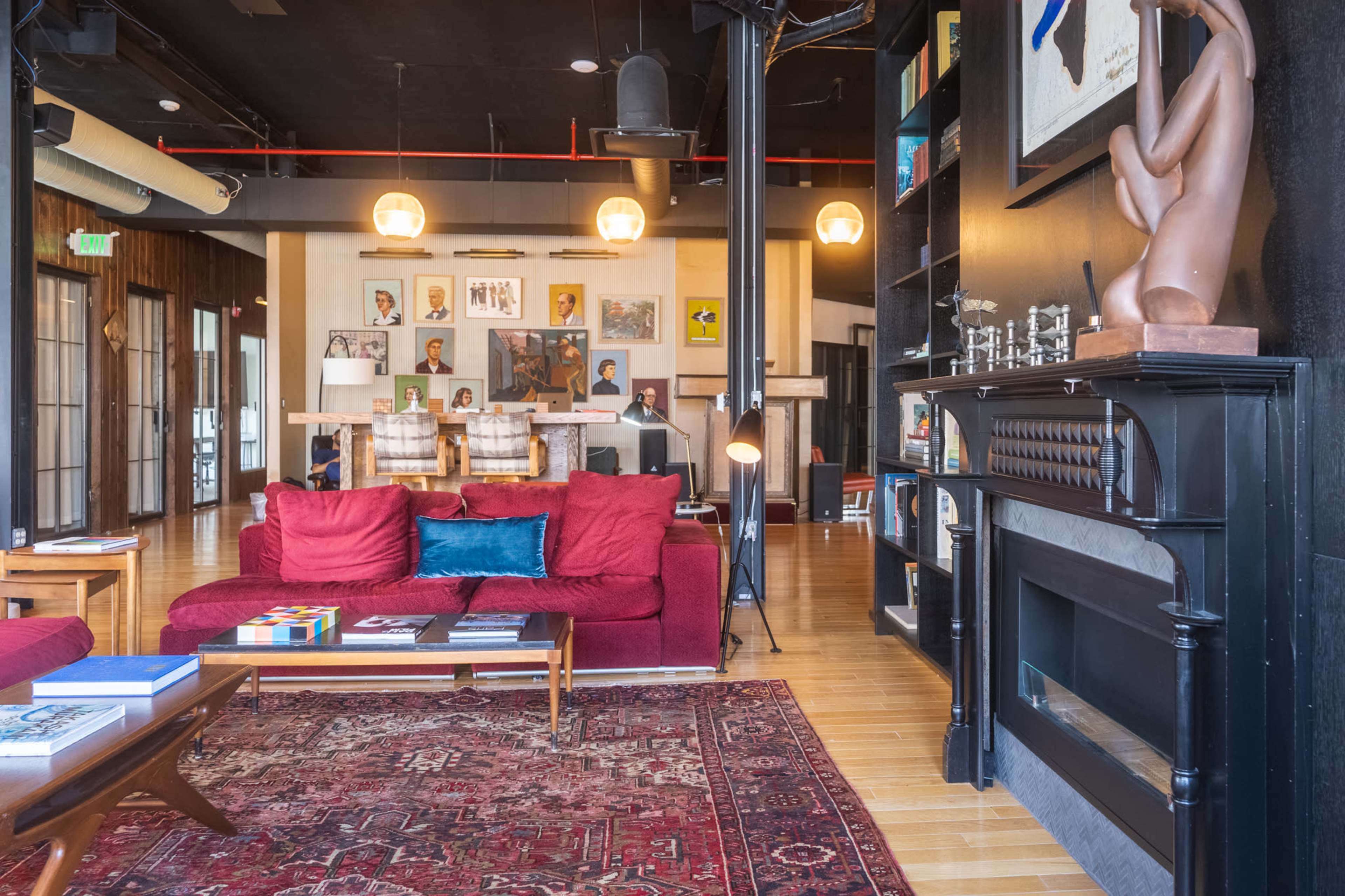 A modern living room features a red plush sofa, a large area rug, and various artworks displayed on the walls.