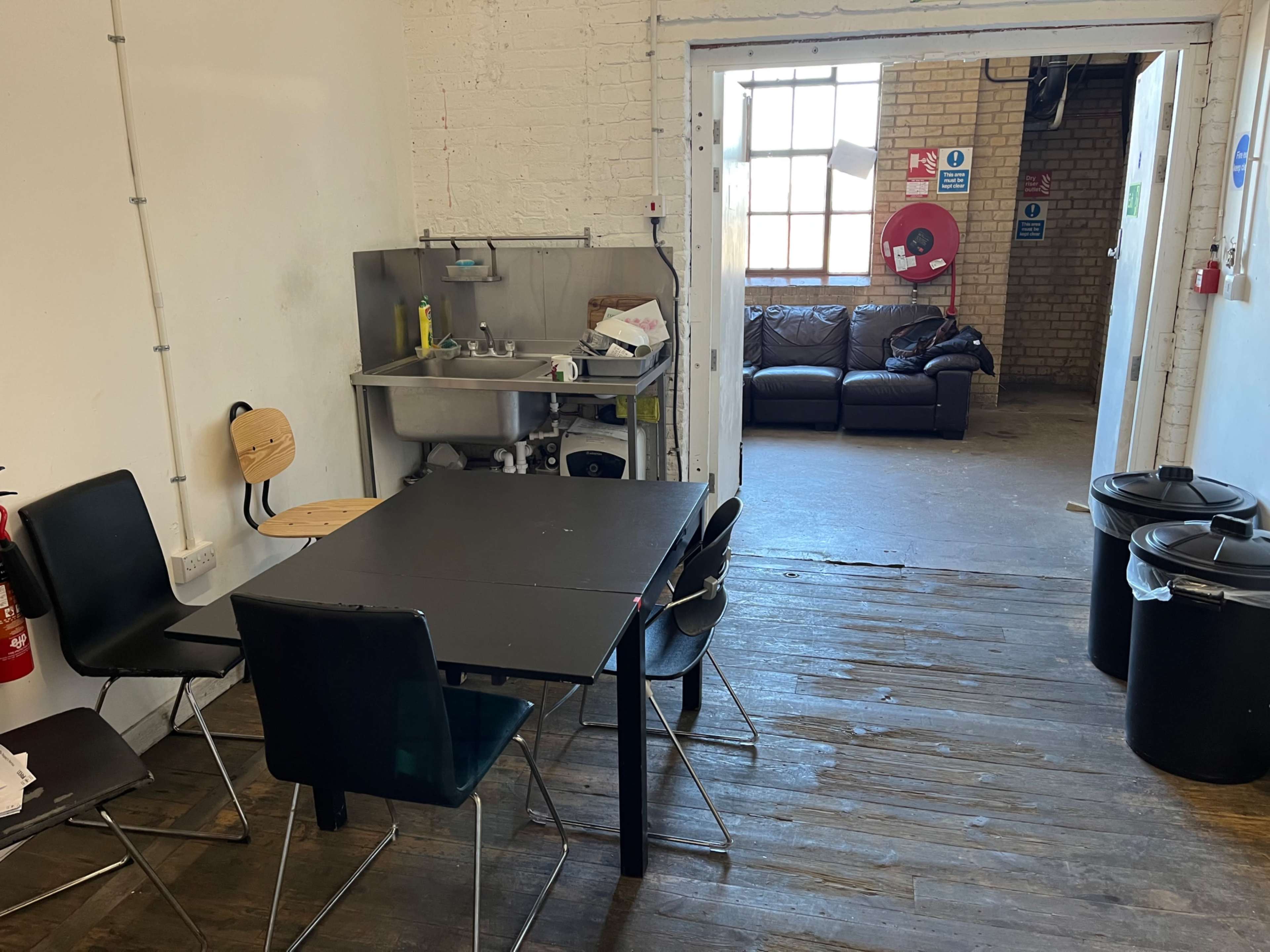 A small kitchen area with a table and chairs, a sink, and a doorway leading to a seating area with a couch.
