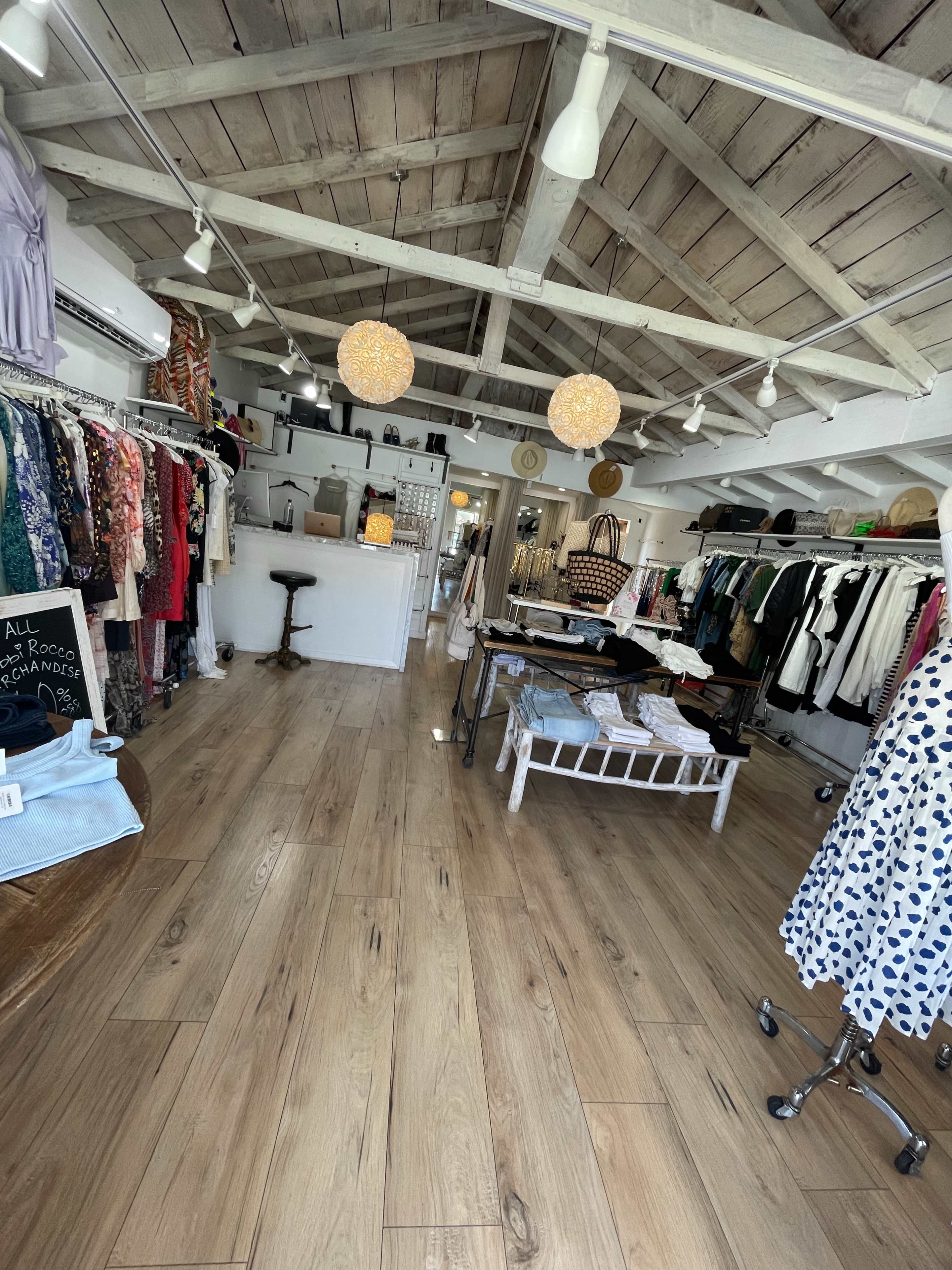 The image shows a clothing boutique with wooden floors, clothing racks on both sides, and a central display area.