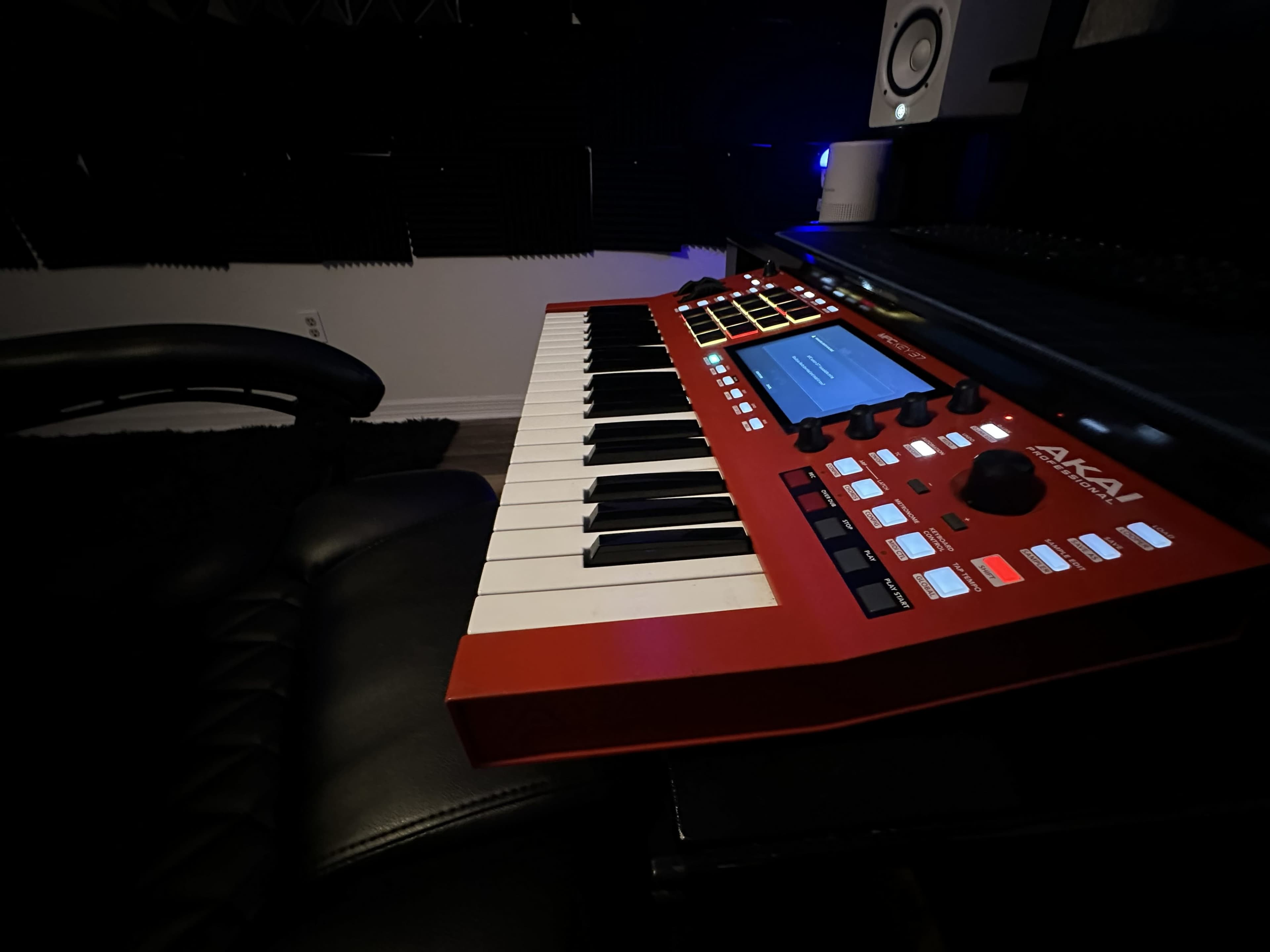 A red AKAI MIDI keyboard is positioned on a dark desk in a music studio.