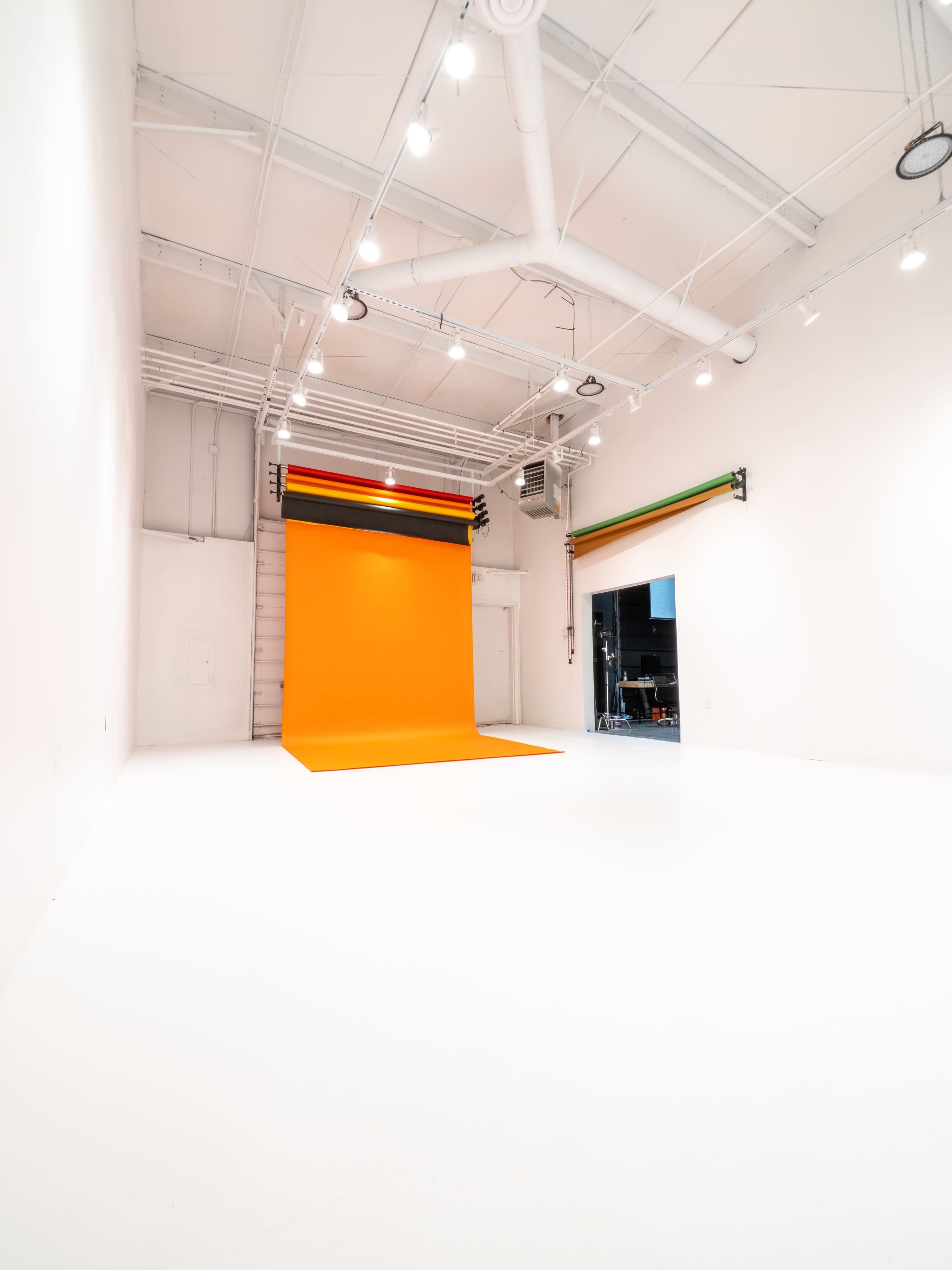 A brightly lit photo studio with a large orange backdrop and white flooring.