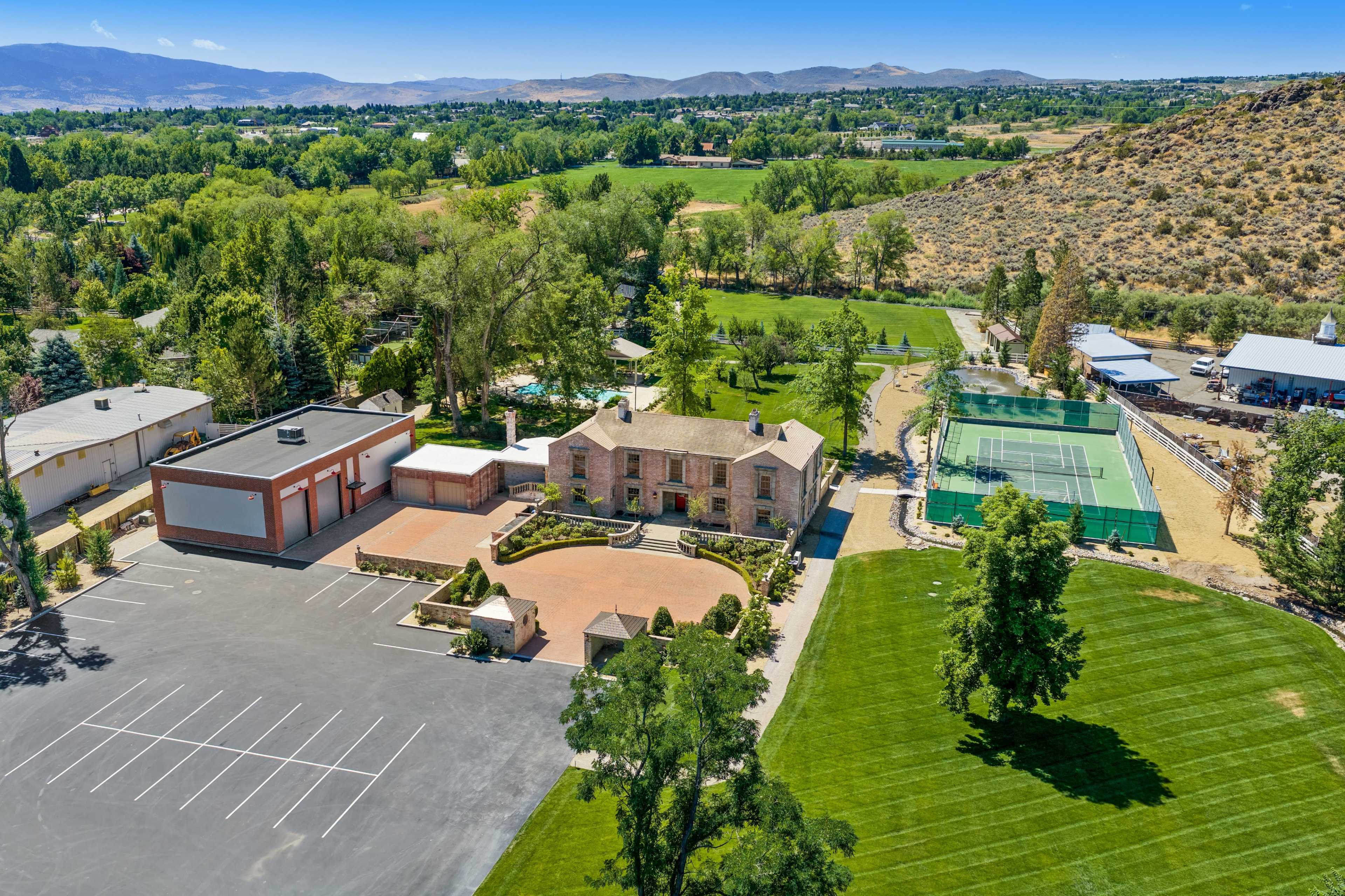 The image shows a large estate featuring a main house, tennis court, and expansive green lawns, surrounded by trees and hills.