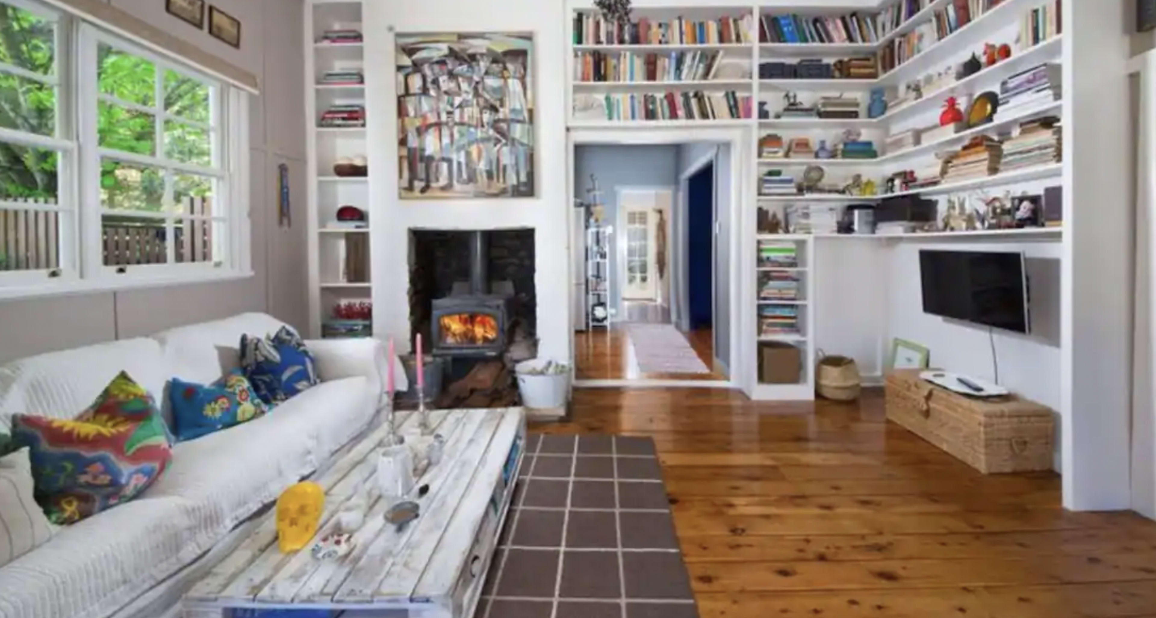 A cozy, well-lit living room features a white sofa, a wooden coffee table, a fireplace, and bookshelves filled with various books and decorative items.