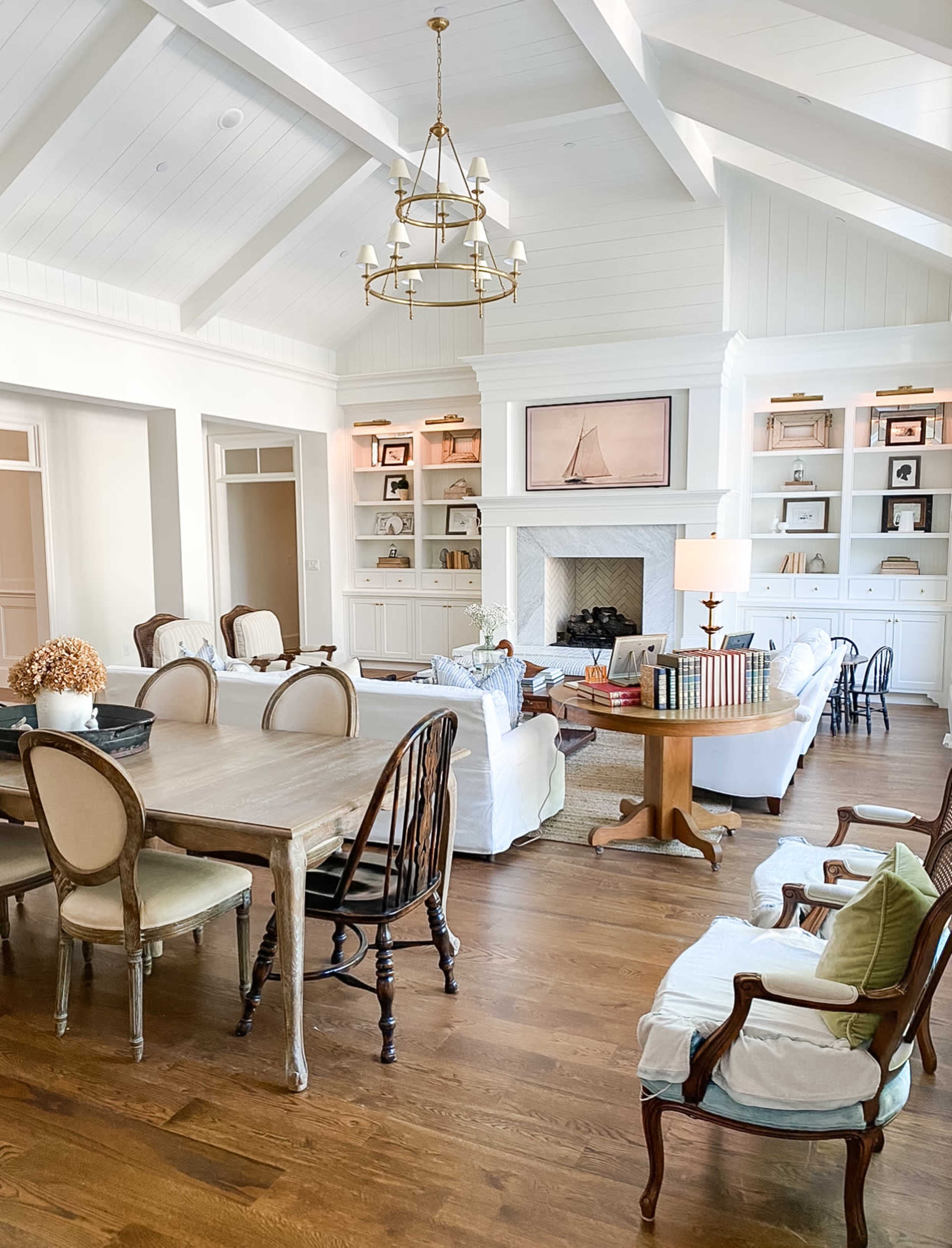 The image shows a spacious, well-lit living area featuring a dining table, several seating arrangements, built-in shelves, and a fireplace.