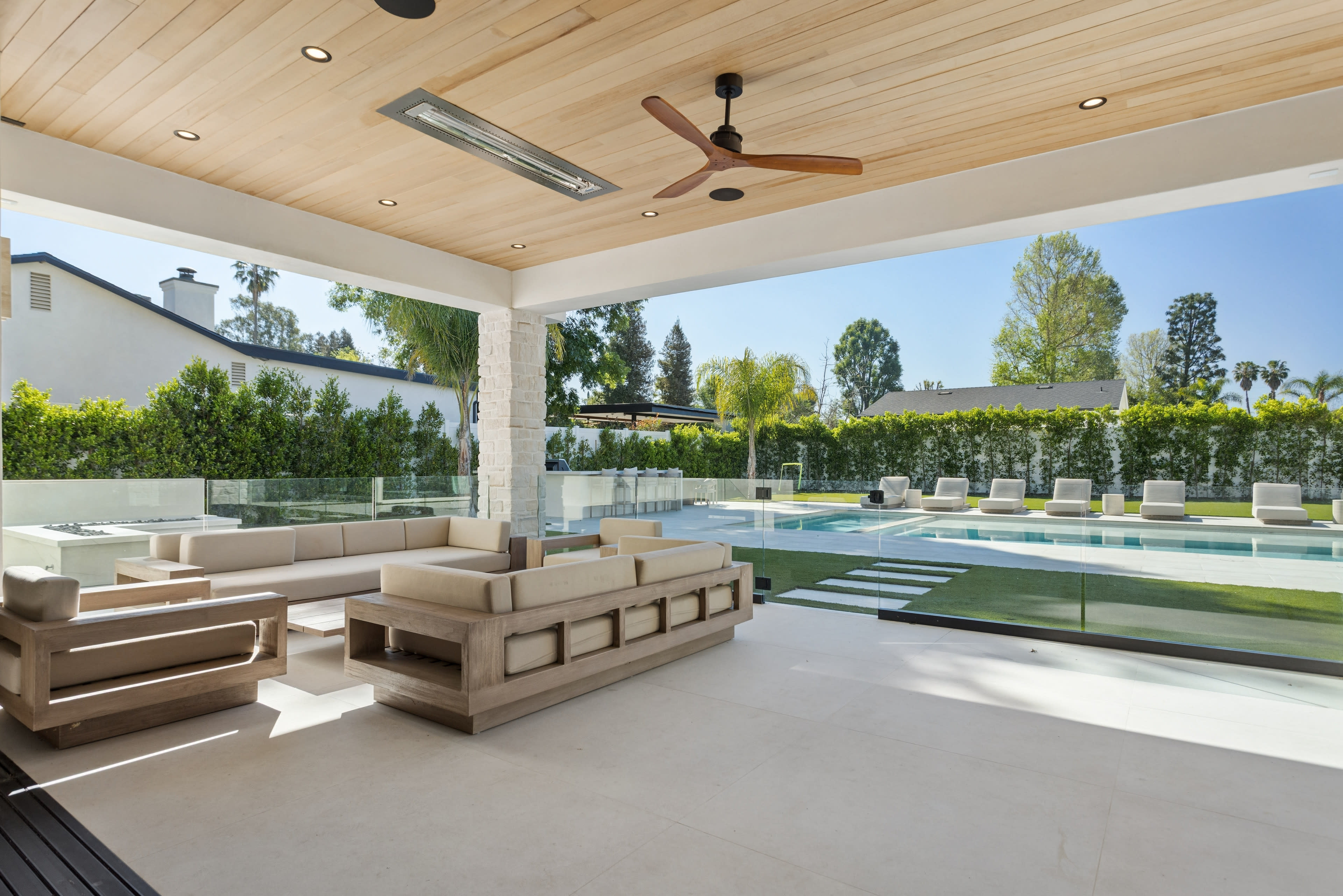 A spacious outdoor living area features a modern seating arrangement and a pool lined with lounge chairs, surrounded by lush greenery.