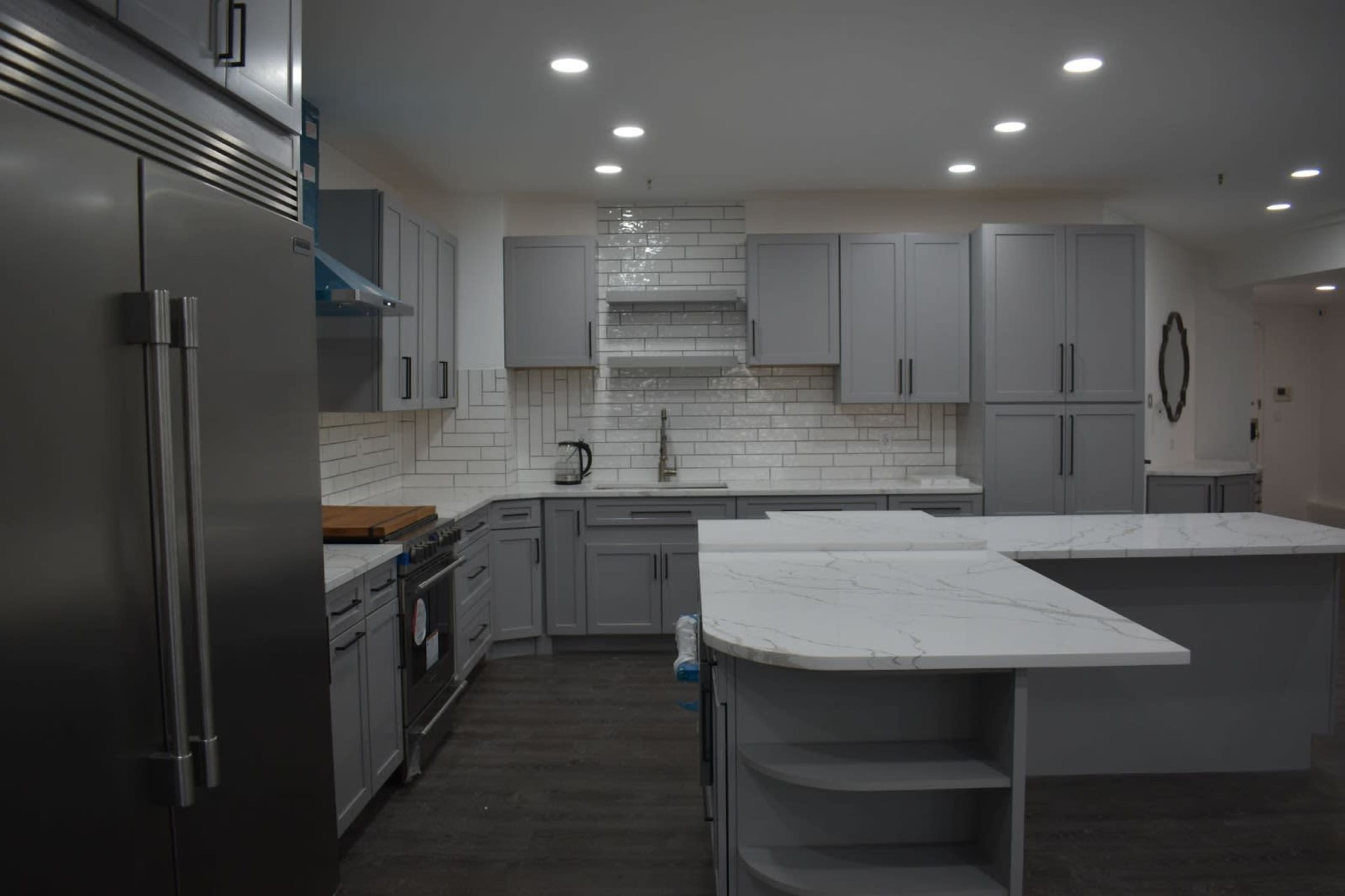 A modern kitchen featuring gray cabinets, a white tiled backsplash, and a central island with a marble countertop.