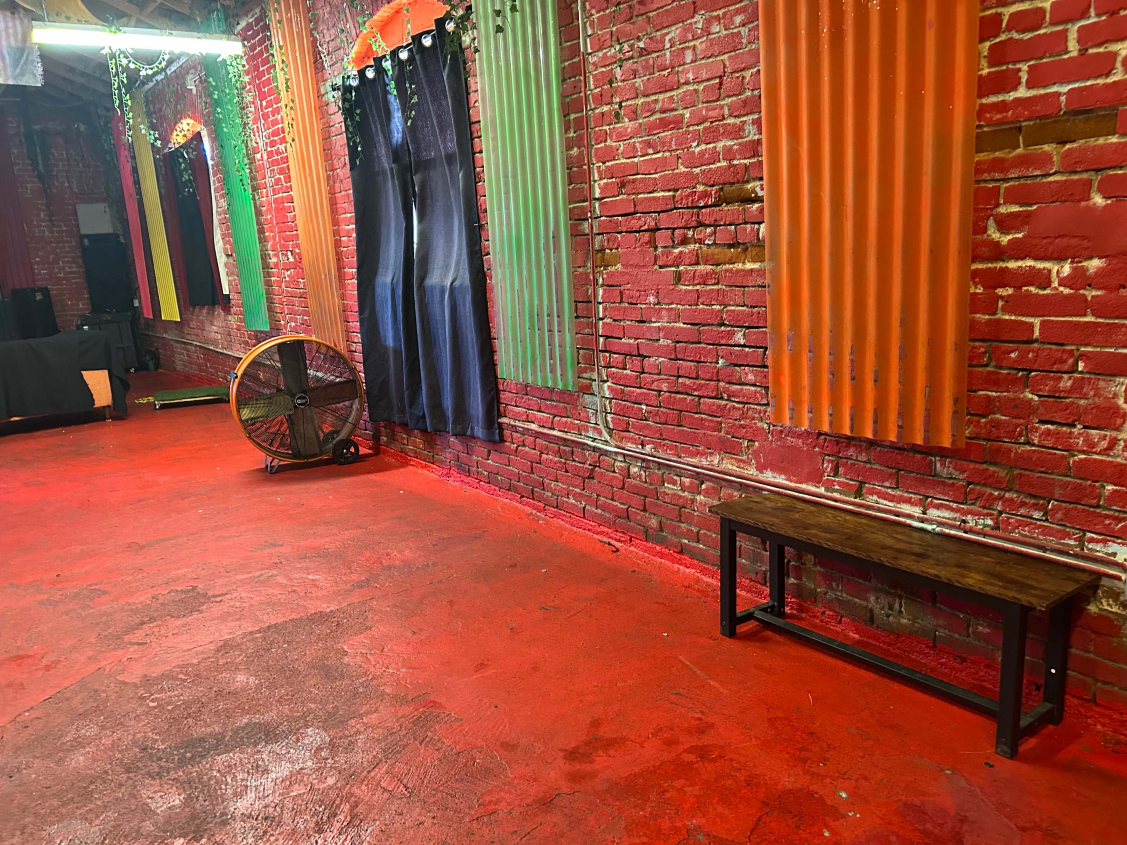 The image shows a red-painted floor in a room with brick walls and colorful corrugated metal and fabric decorations.
