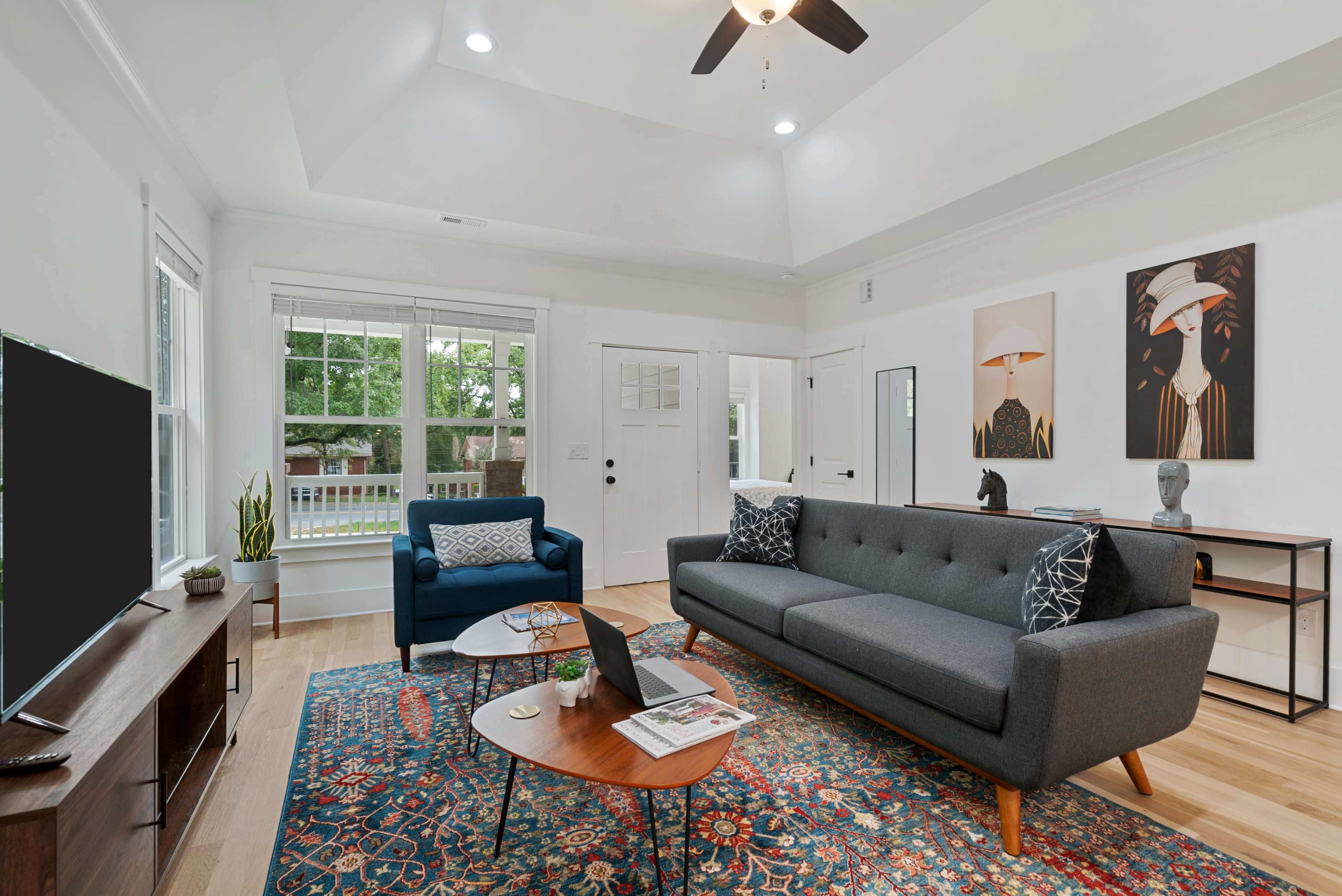 A modern living room featuring a gray sectional sofa, an accent chair, a coffee table, and two artwork pieces on the walls, illuminated by natural light from the windows.