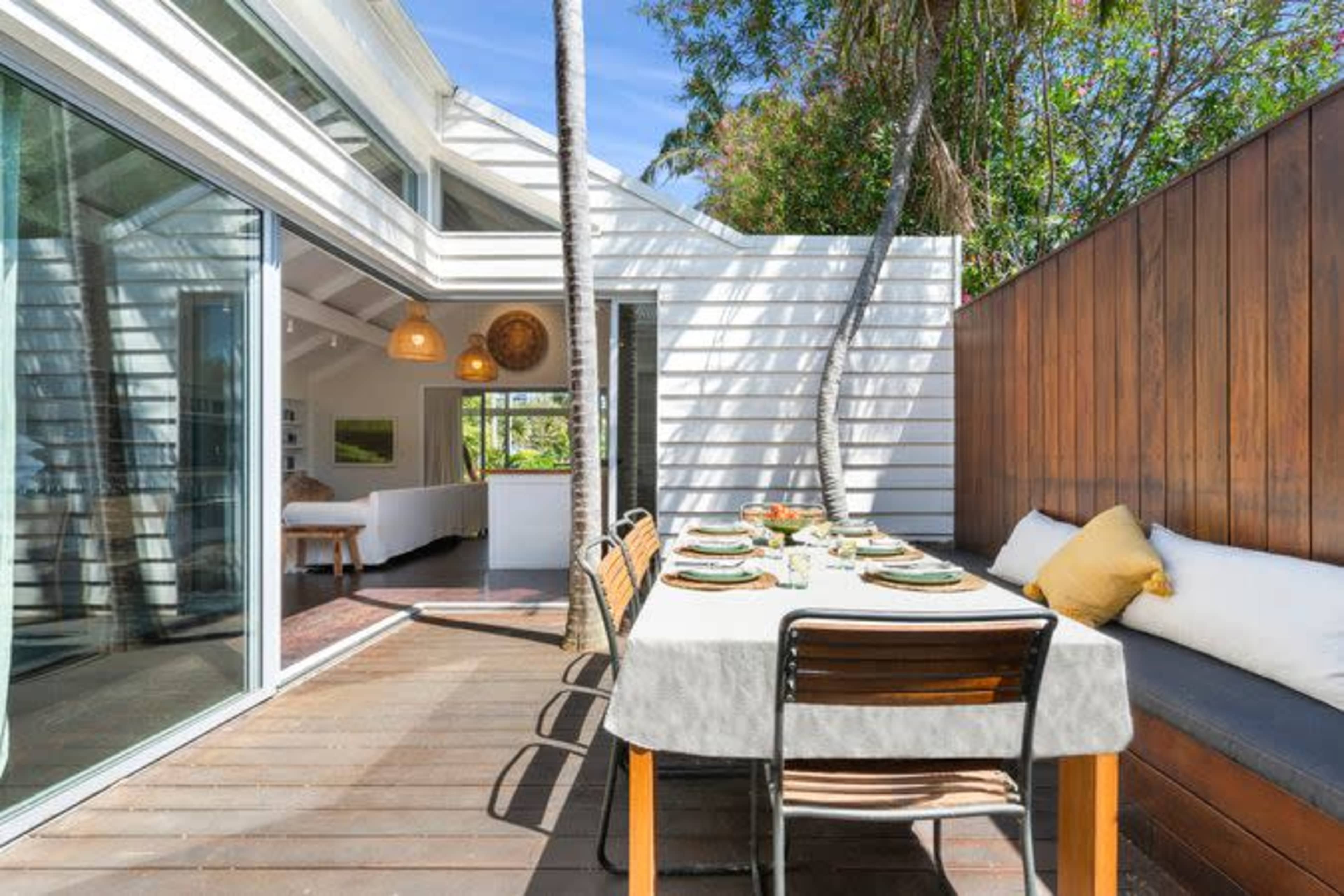 A spacious outdoor dining area is set with a table and chairs, surrounded by modern architecture and greenery.
