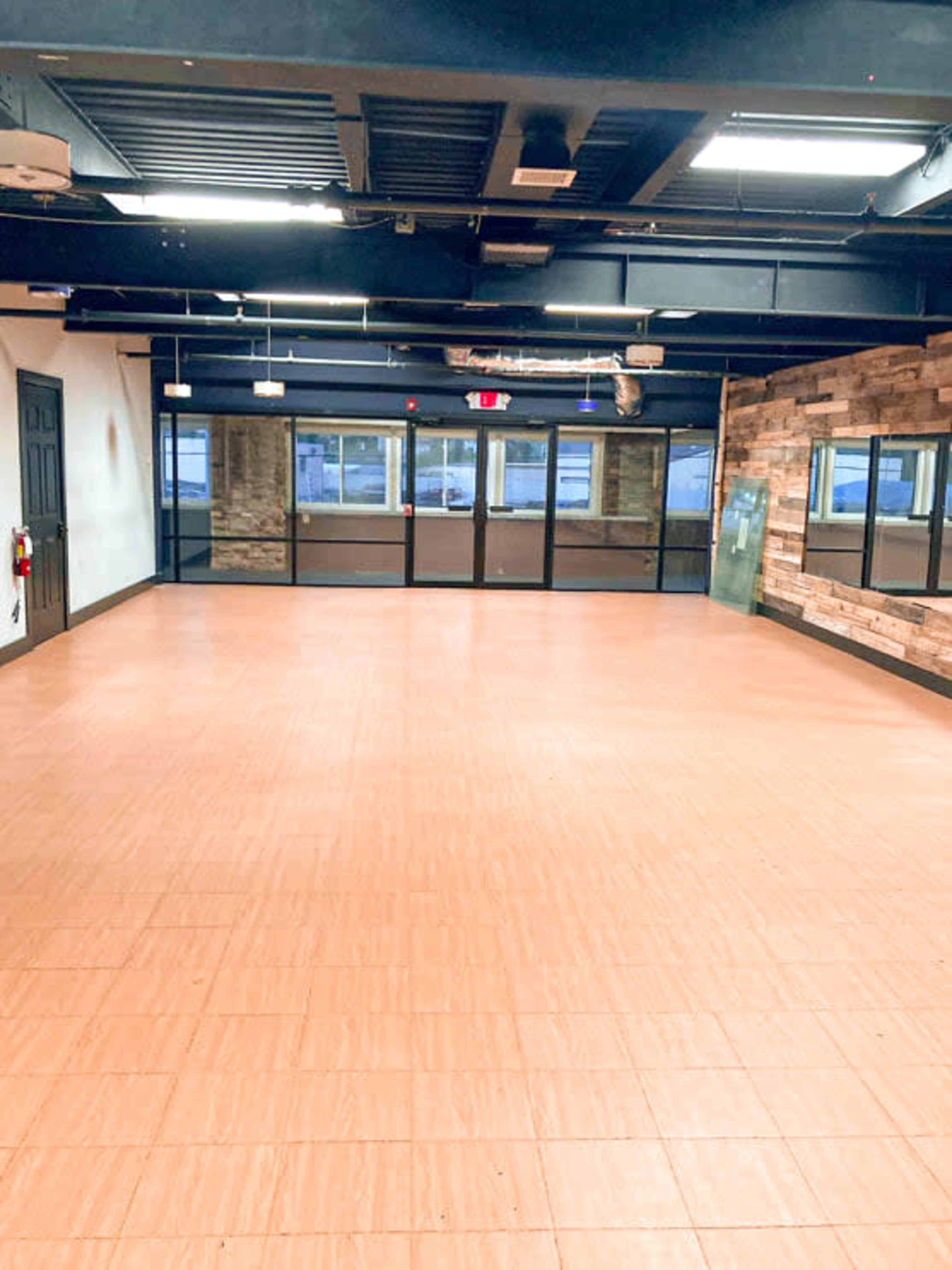 An empty interior space with a tiled floor, black ceiling, and large glass windows.