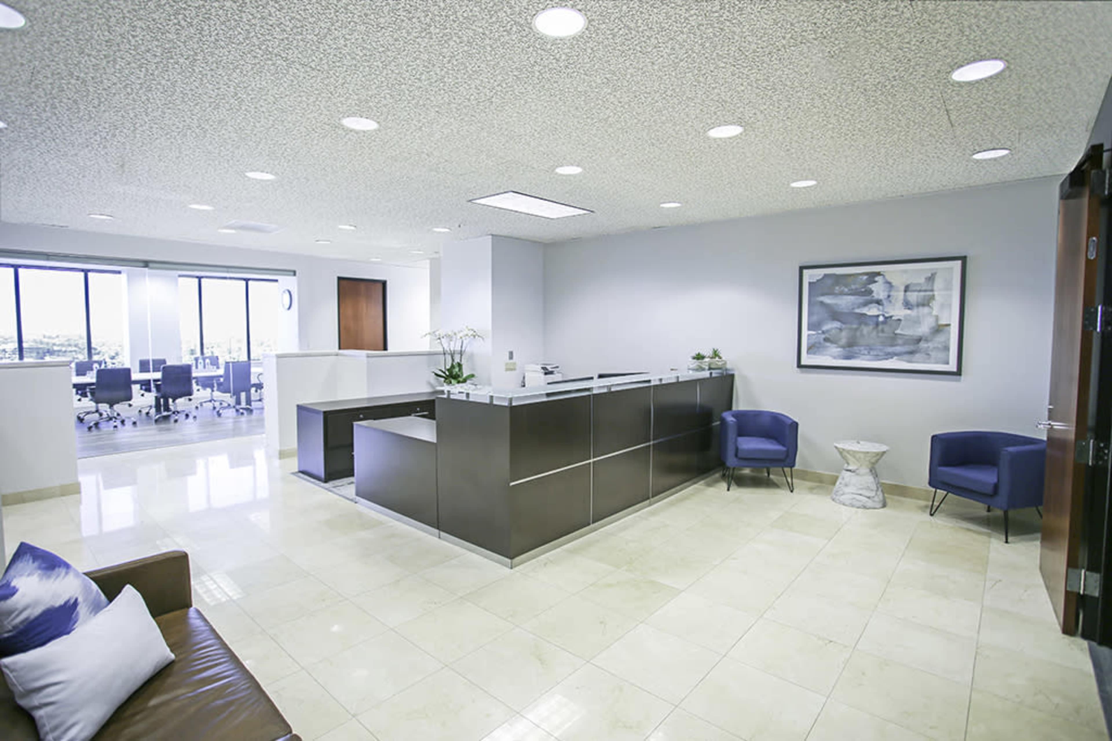 A modern office reception area with a desk, chairs, and a view of a conference room in the background.