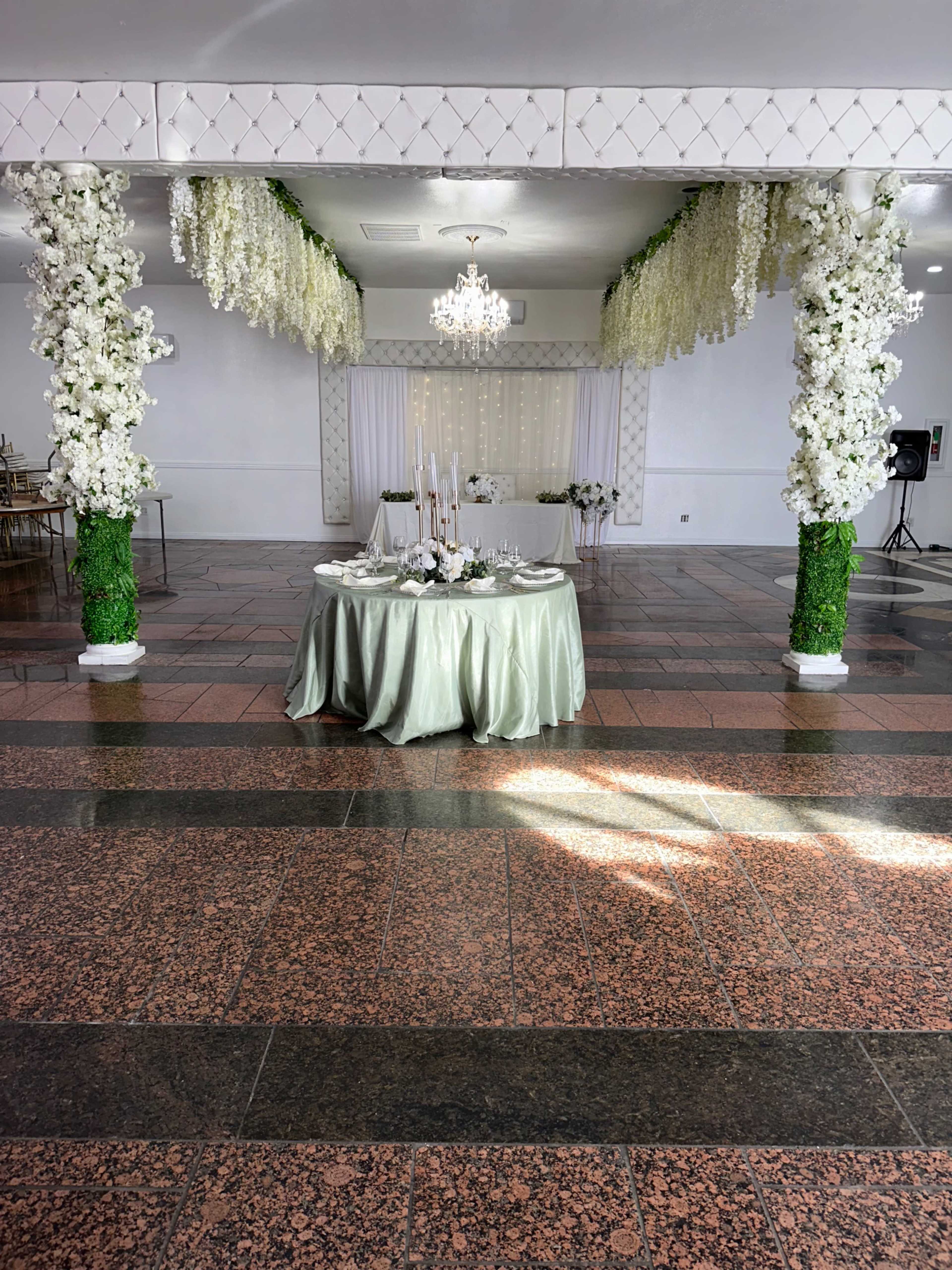 The image showcases a decorated event space featuring floral arrangements on columns, a beautifully set dining table, and elegant decor.