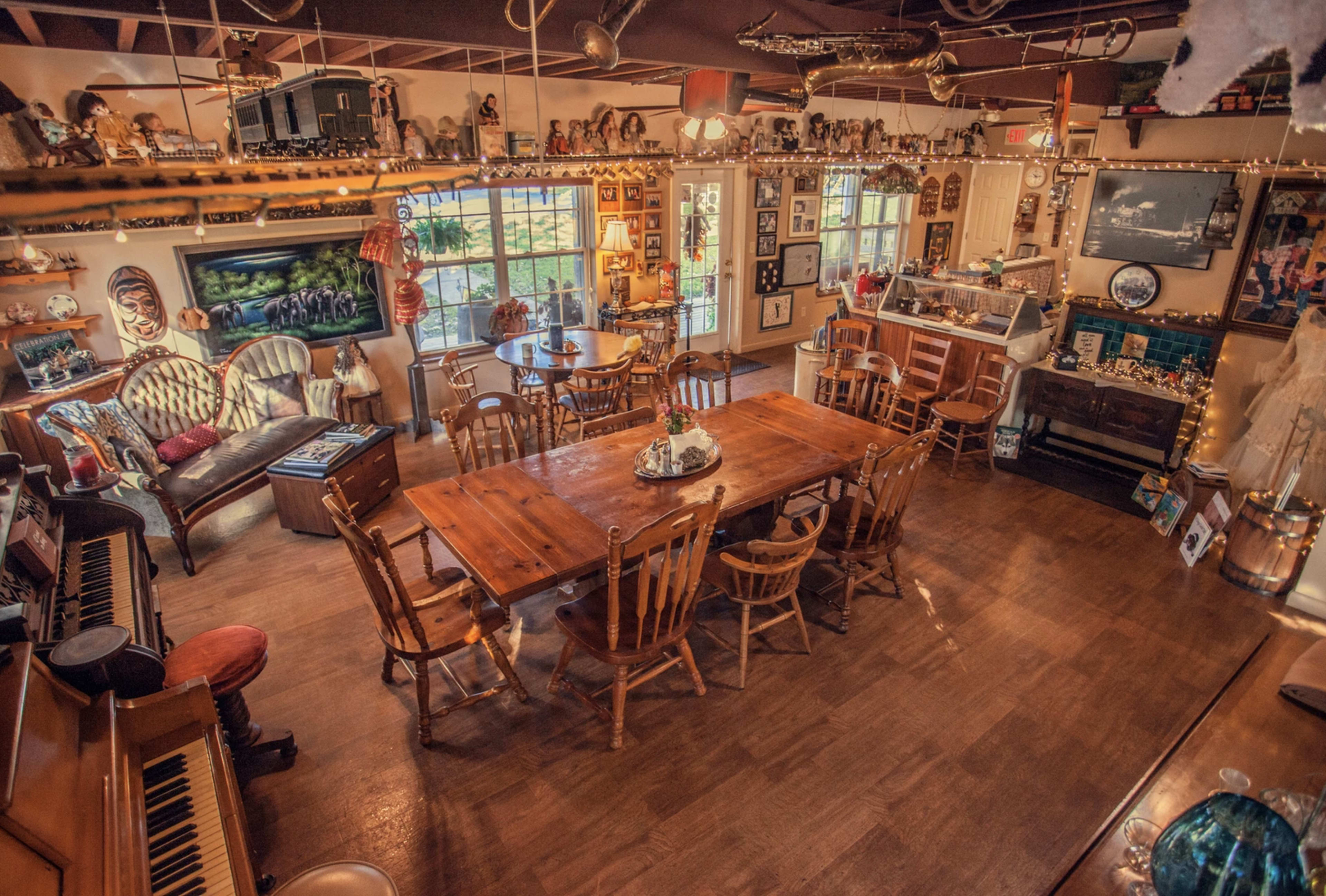 A cozy dining area filled with wooden tables and chairs, featuring eclectic decor on the walls and a piano in one corner.