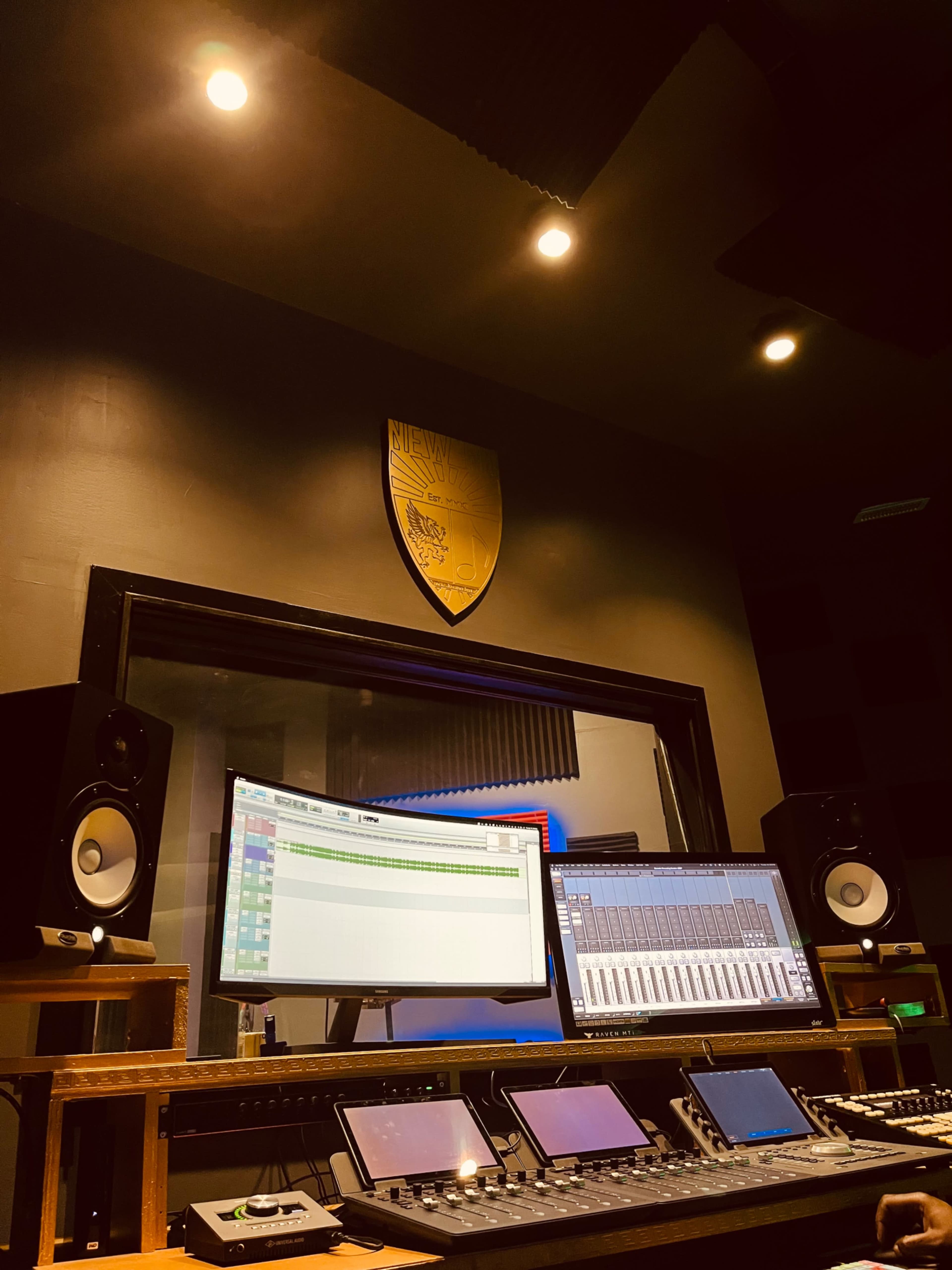 A modern audio recording studio with a large control desk, multiple monitors, and soundproofing panels on the walls.