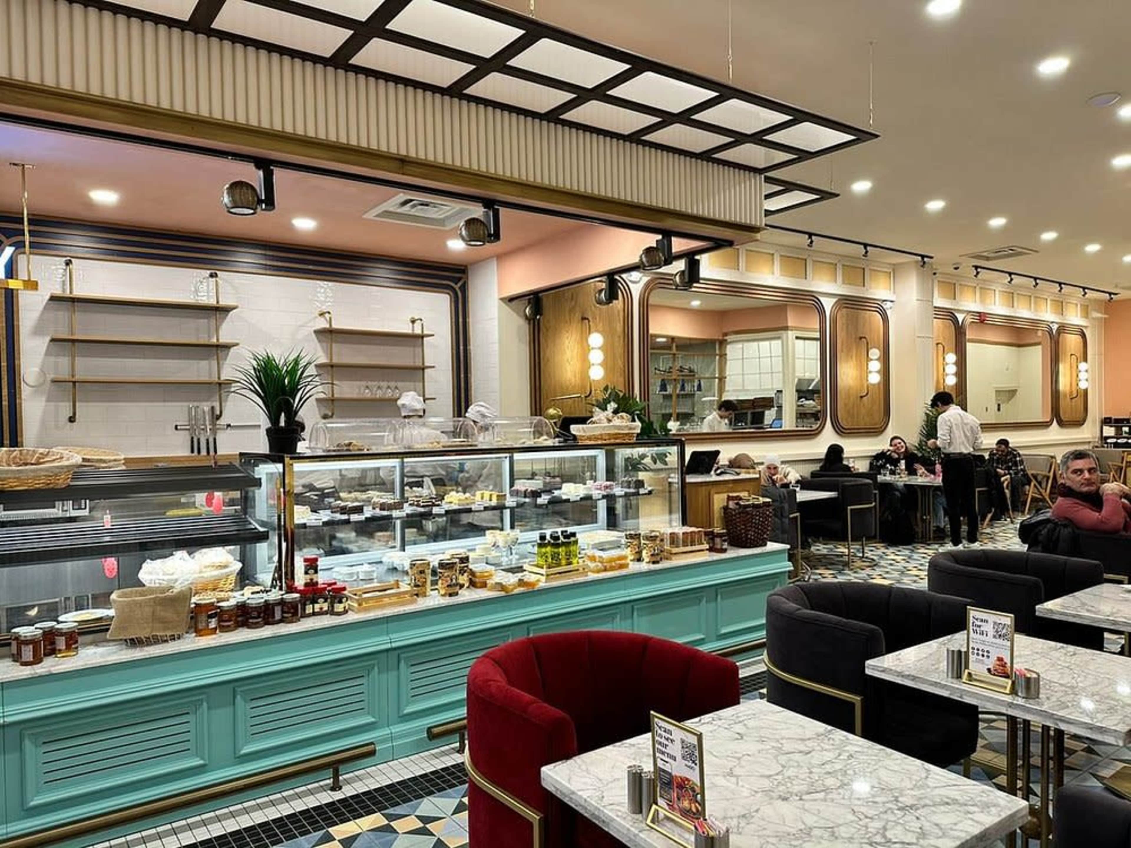 The image shows a modern café interior featuring a display counter with pastries and desserts, elegant seating arrangements, and decorative lighting.