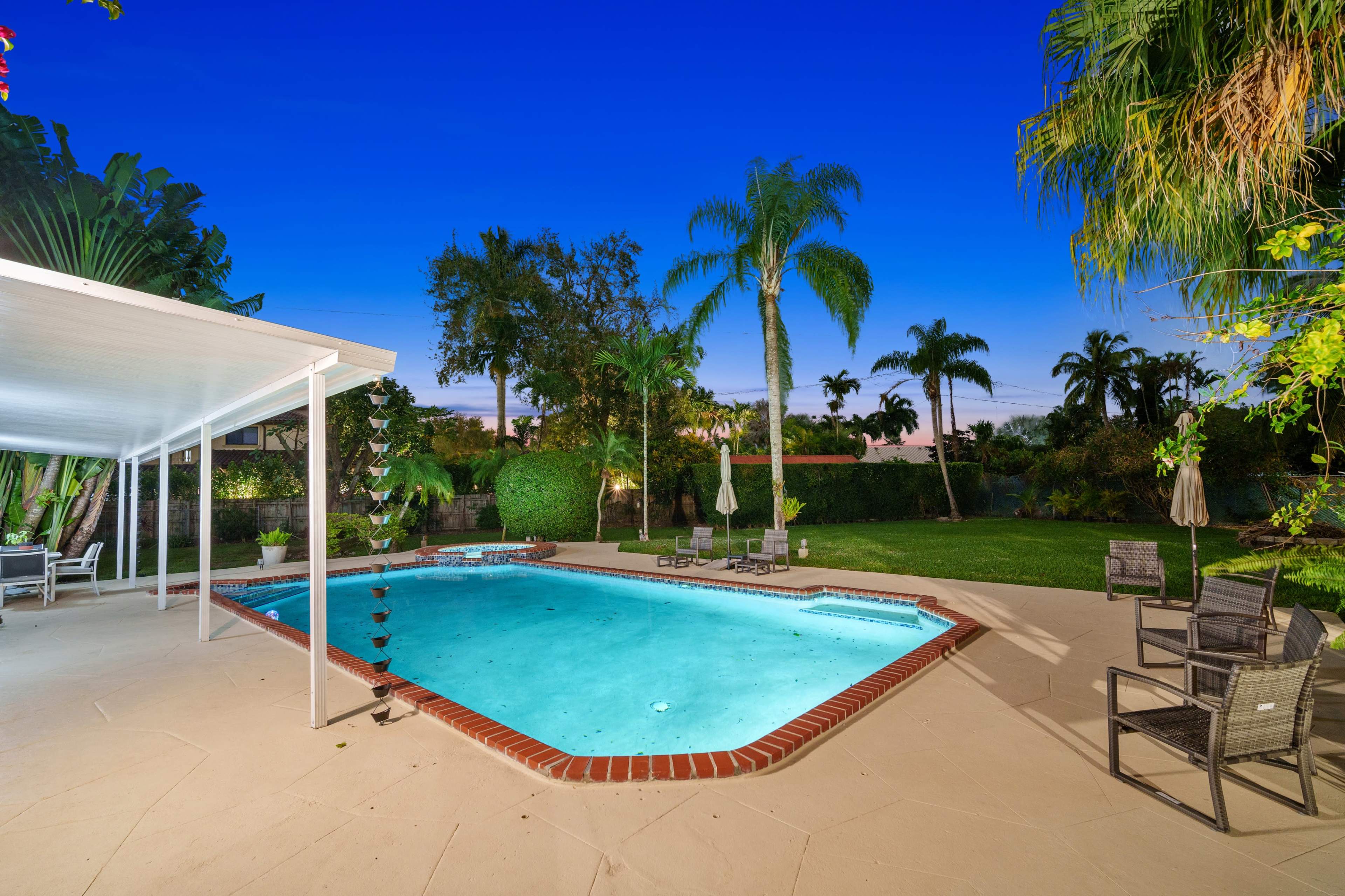 The image shows a backyard swimming pool bordered by palm trees and lounge chairs under a clear evening sky.