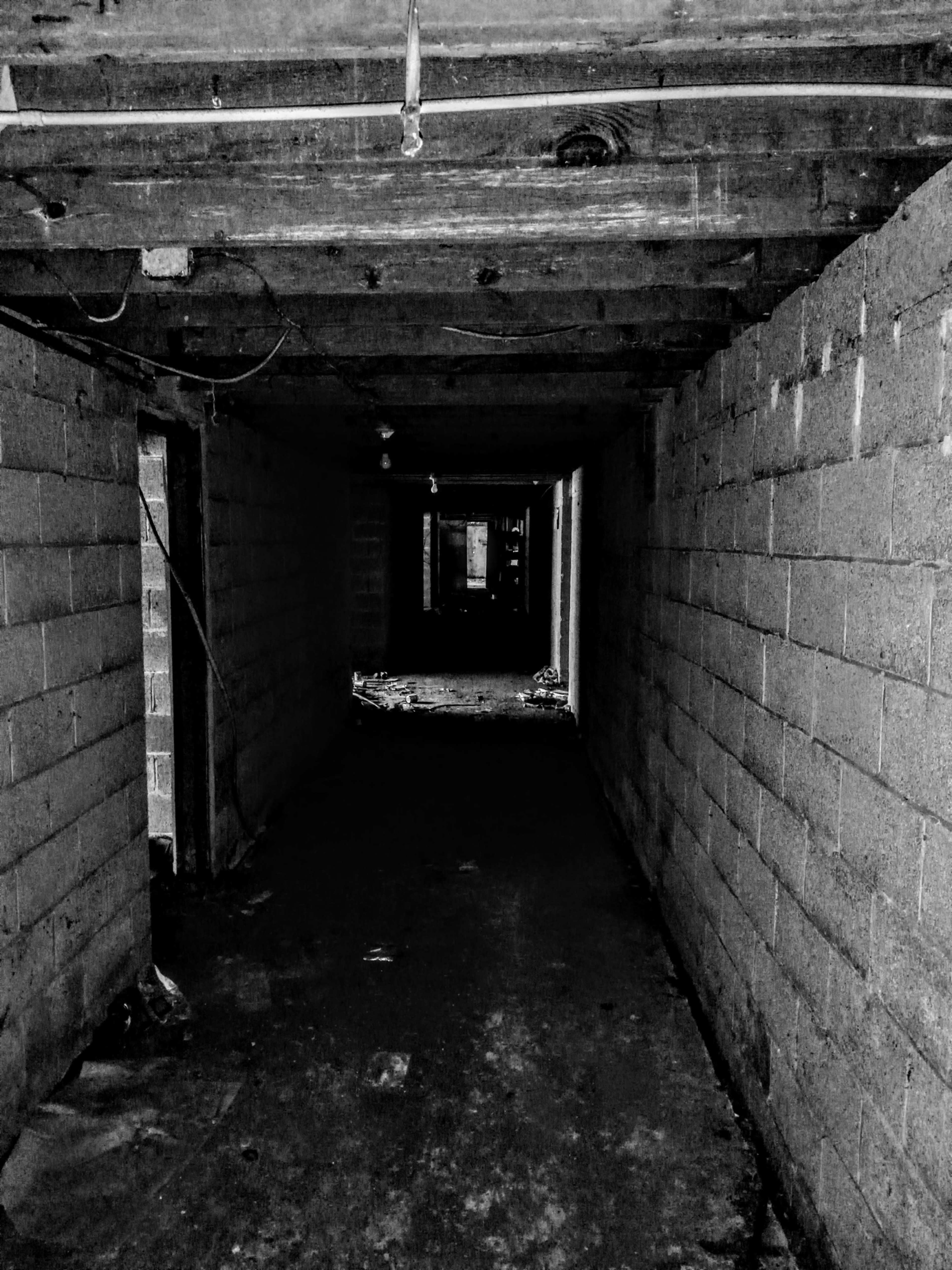 A dimly lit underground corridor features gray block walls and exposed wooden beams overhead.
