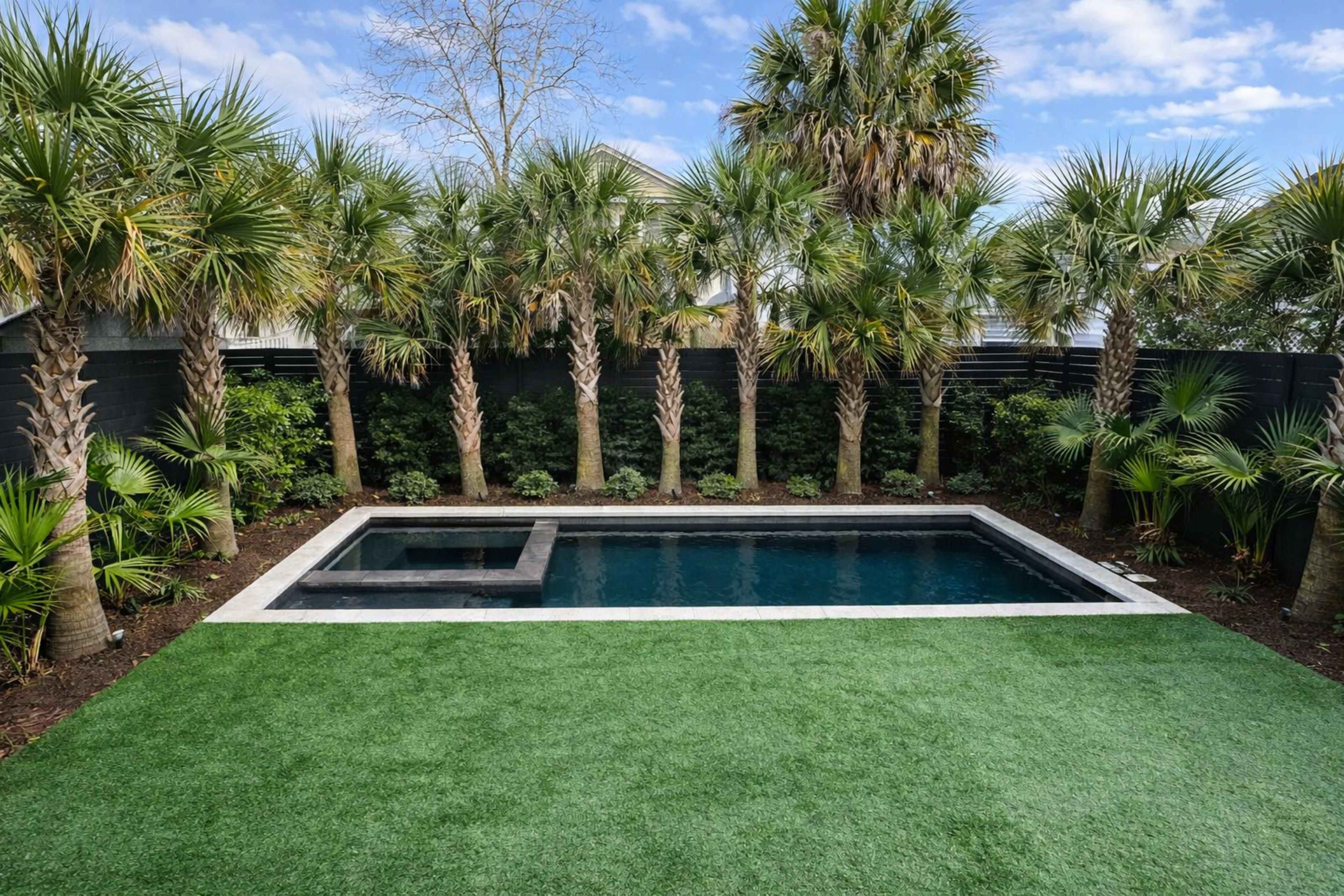 The image shows a backyard with a rectangular swimming pool surrounded by palm trees and artificial grass.